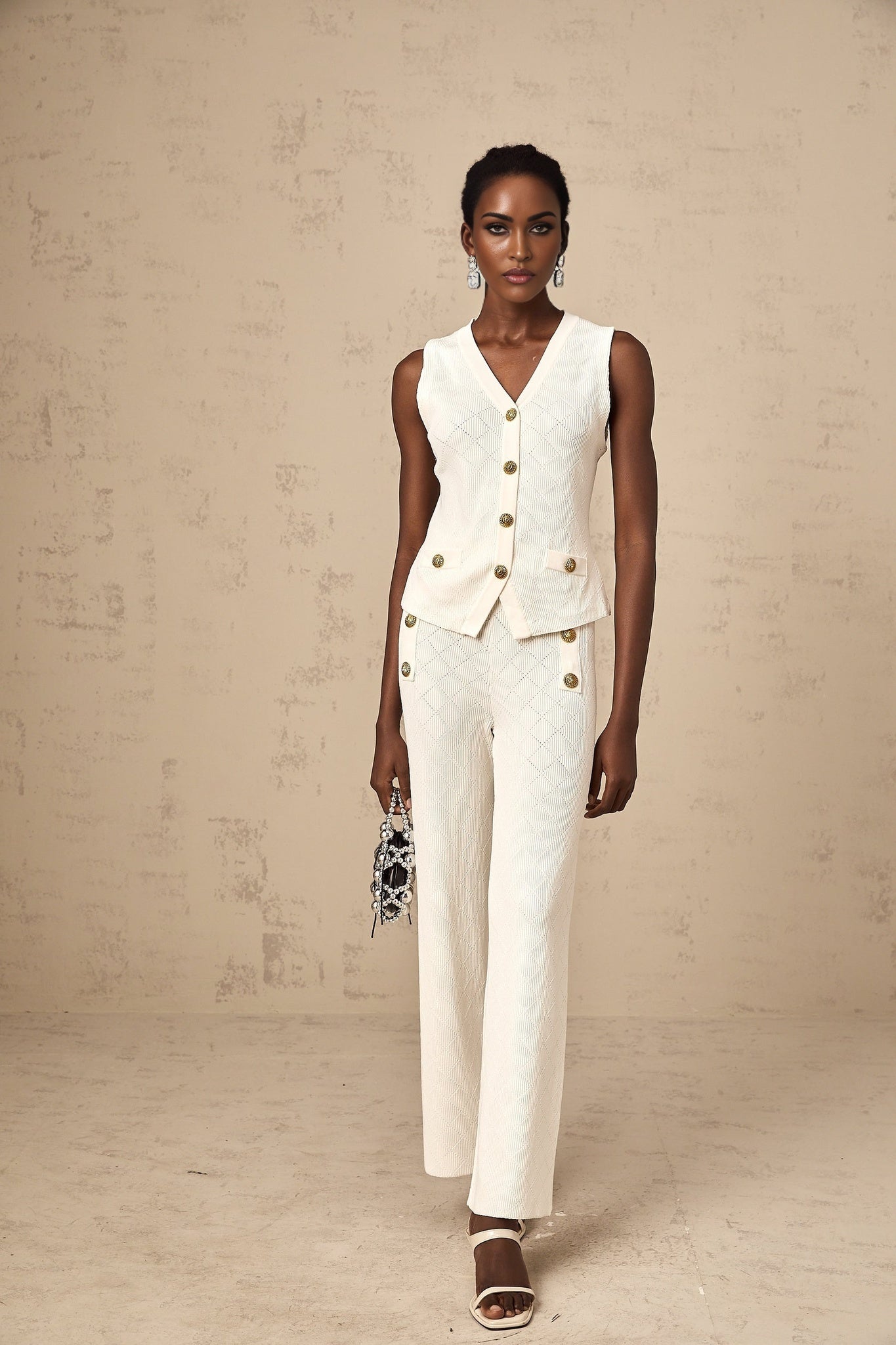 Woman wearing white knitted sleeveless top and matching wide leg trousers standing in relaxed pose