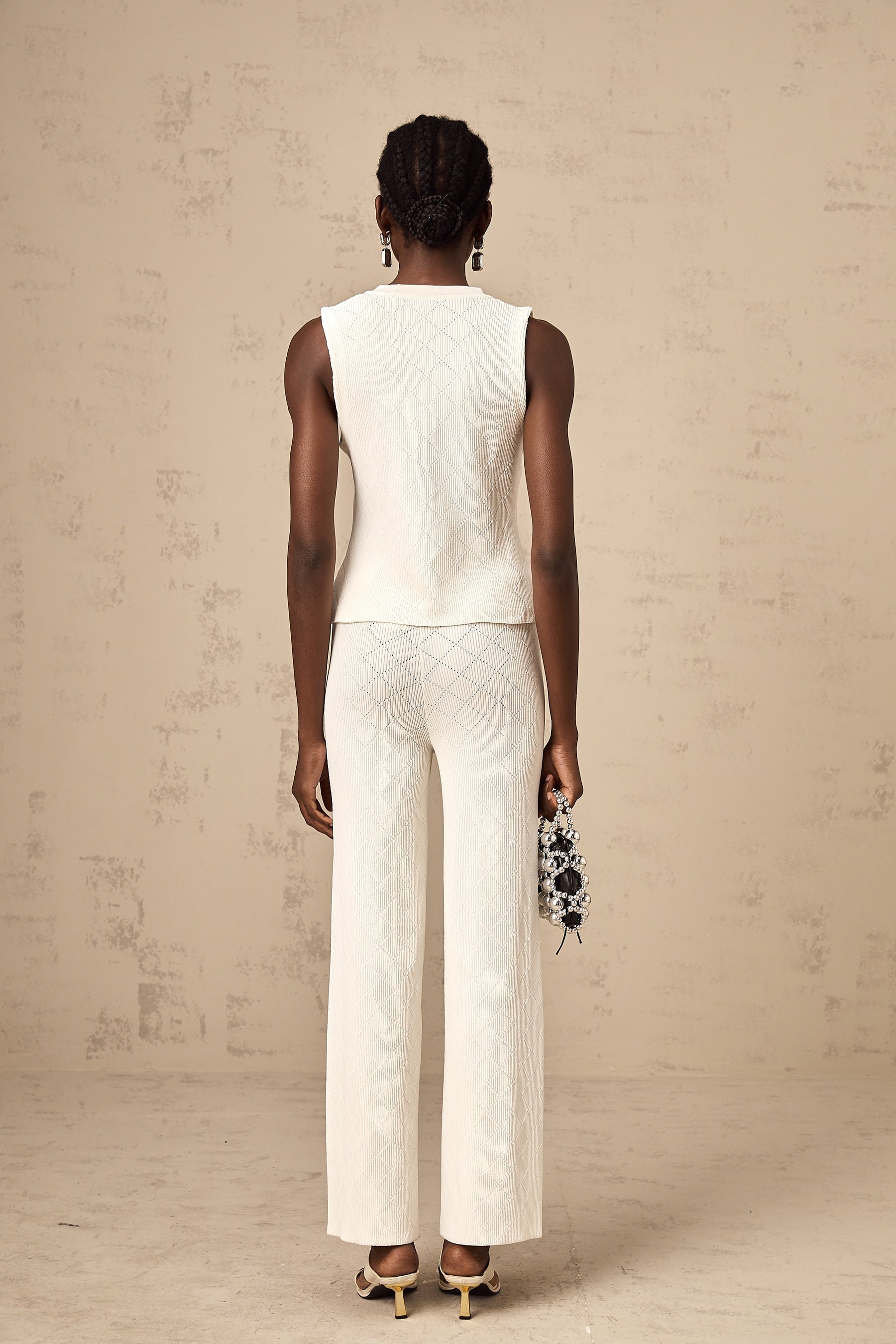 Woman wearing white knitted top and matching trousers standing in relaxed pose against plain background