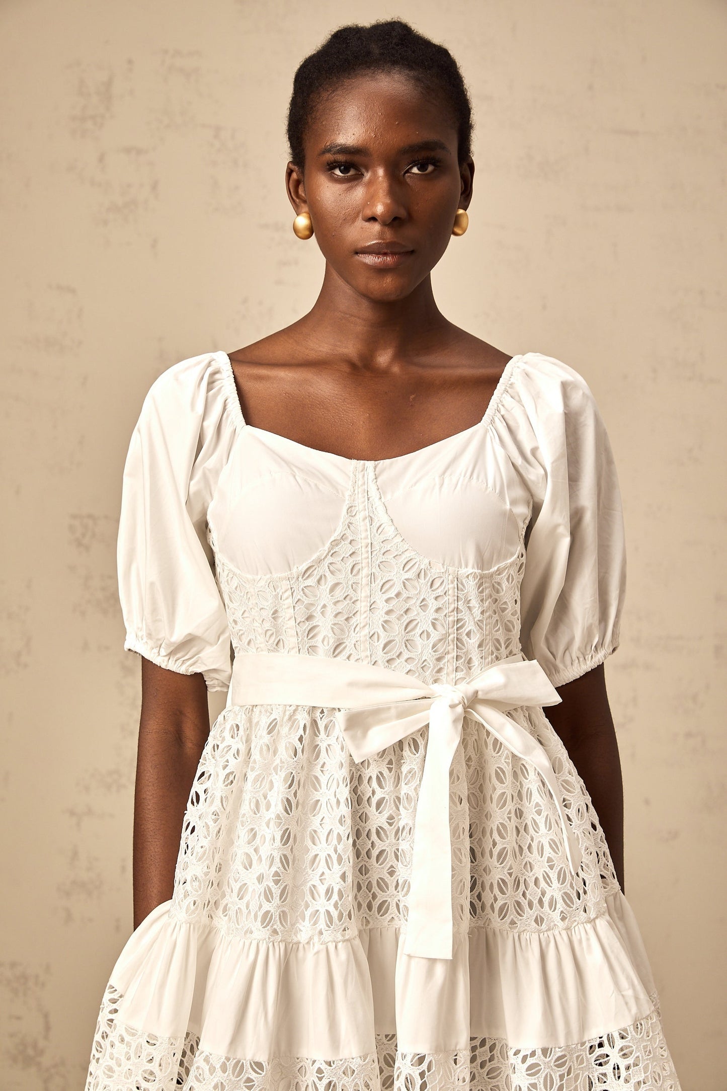 Woman wearing white lace midi dress with tiered skirt and corded lace details standing in front of neutral background