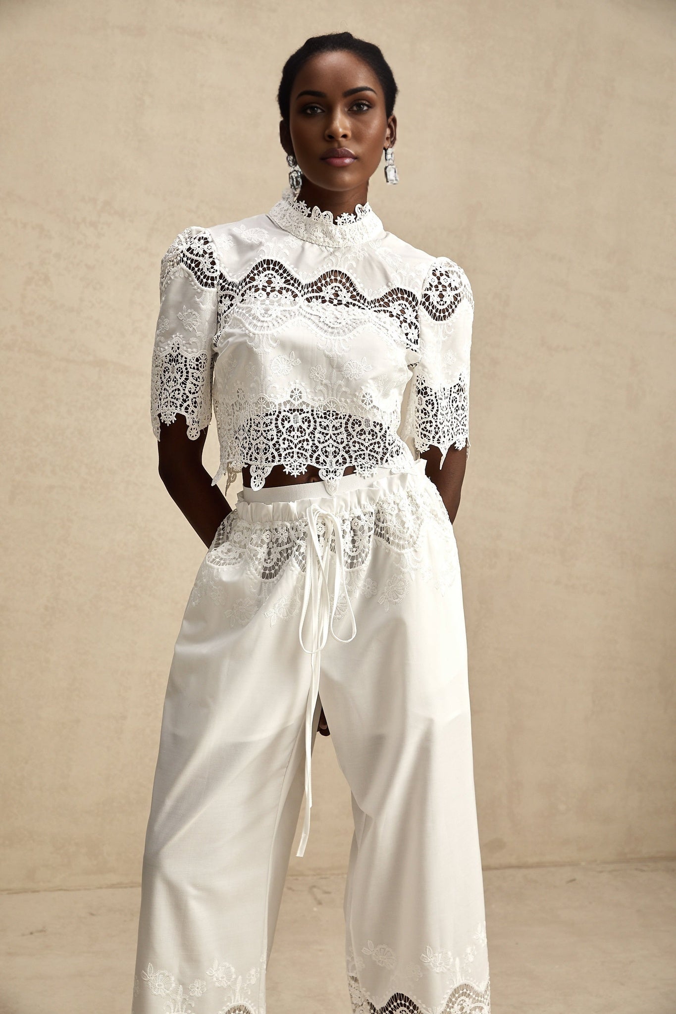 Woman wearing white lace trim cropped top and matching trousers with cutout details Raphaelle matching set