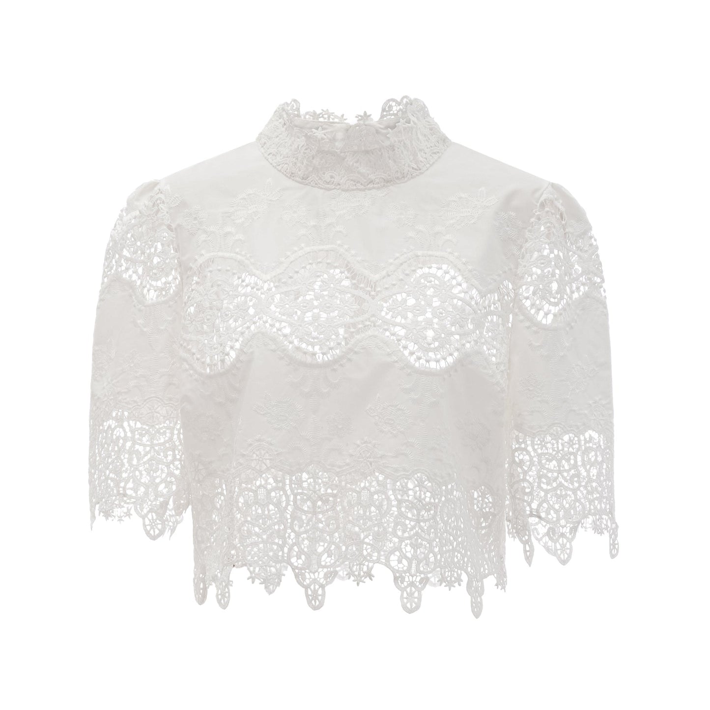 Woman wearing white lace trim cropped top and matching trousers with cutout details standing against plain background