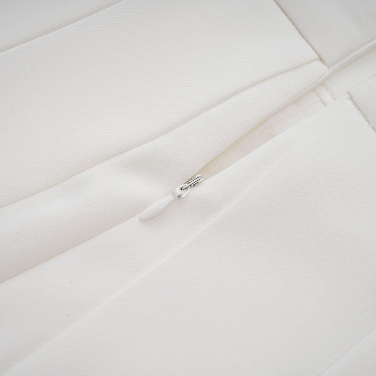 Woman wearing white matching set with creased top and trousers standing against plain background