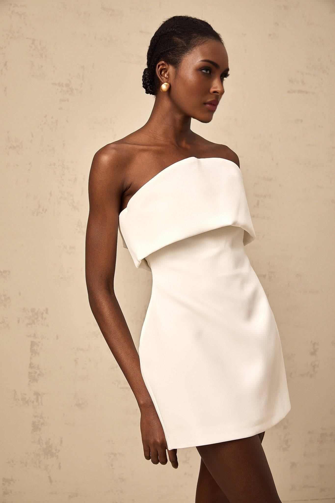 Woman wearing white off shoulder mini dress with puff sleeves standing against plain background