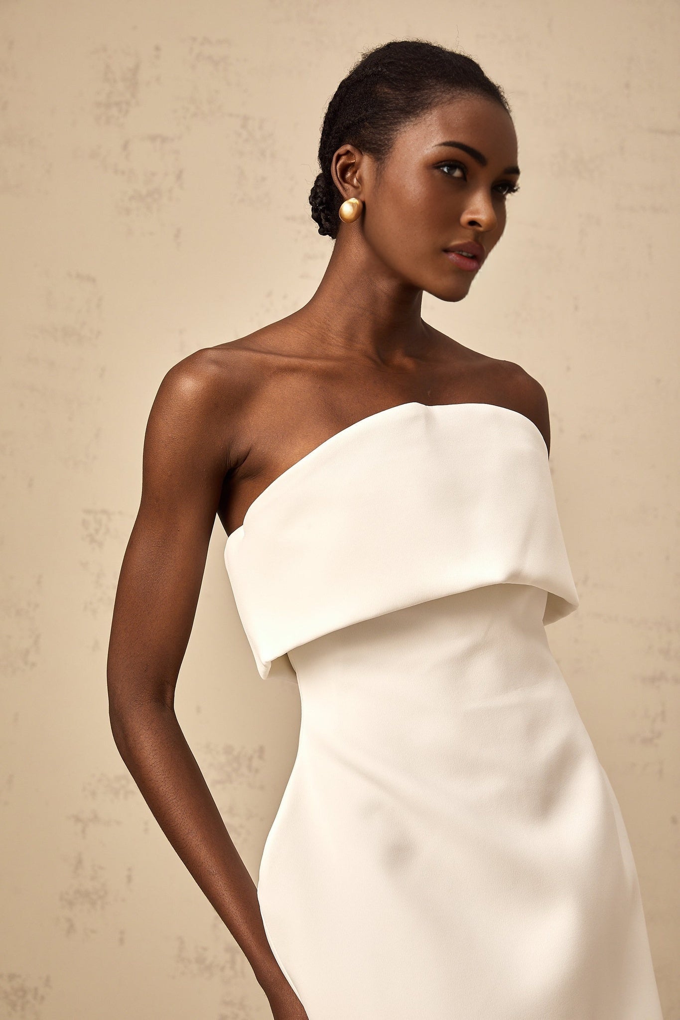 Woman wearing white offshoulder mini dress with puffed sleeves standing against plain background