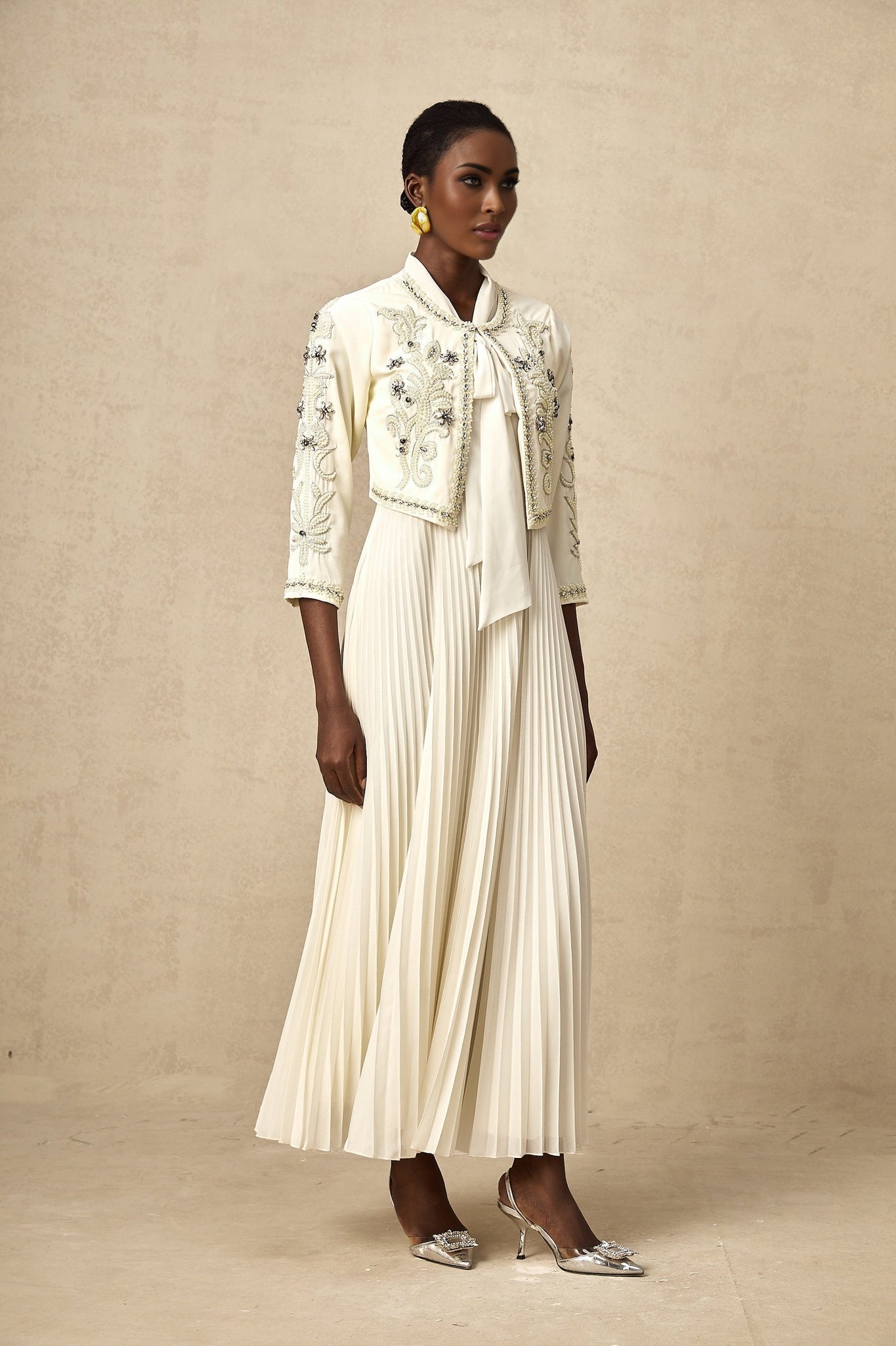 Woman wearing white pleated dress with matching embellished jacket formal outfit set