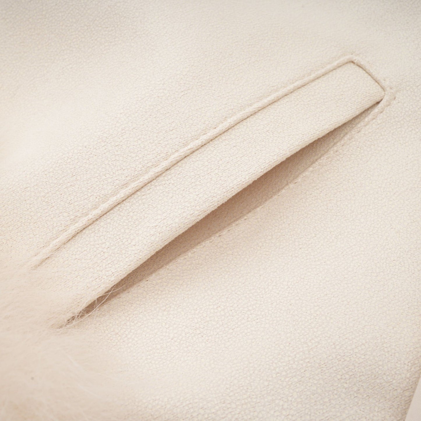 Woman wearing white suede short coat with fur trim and padded design standing against plain background