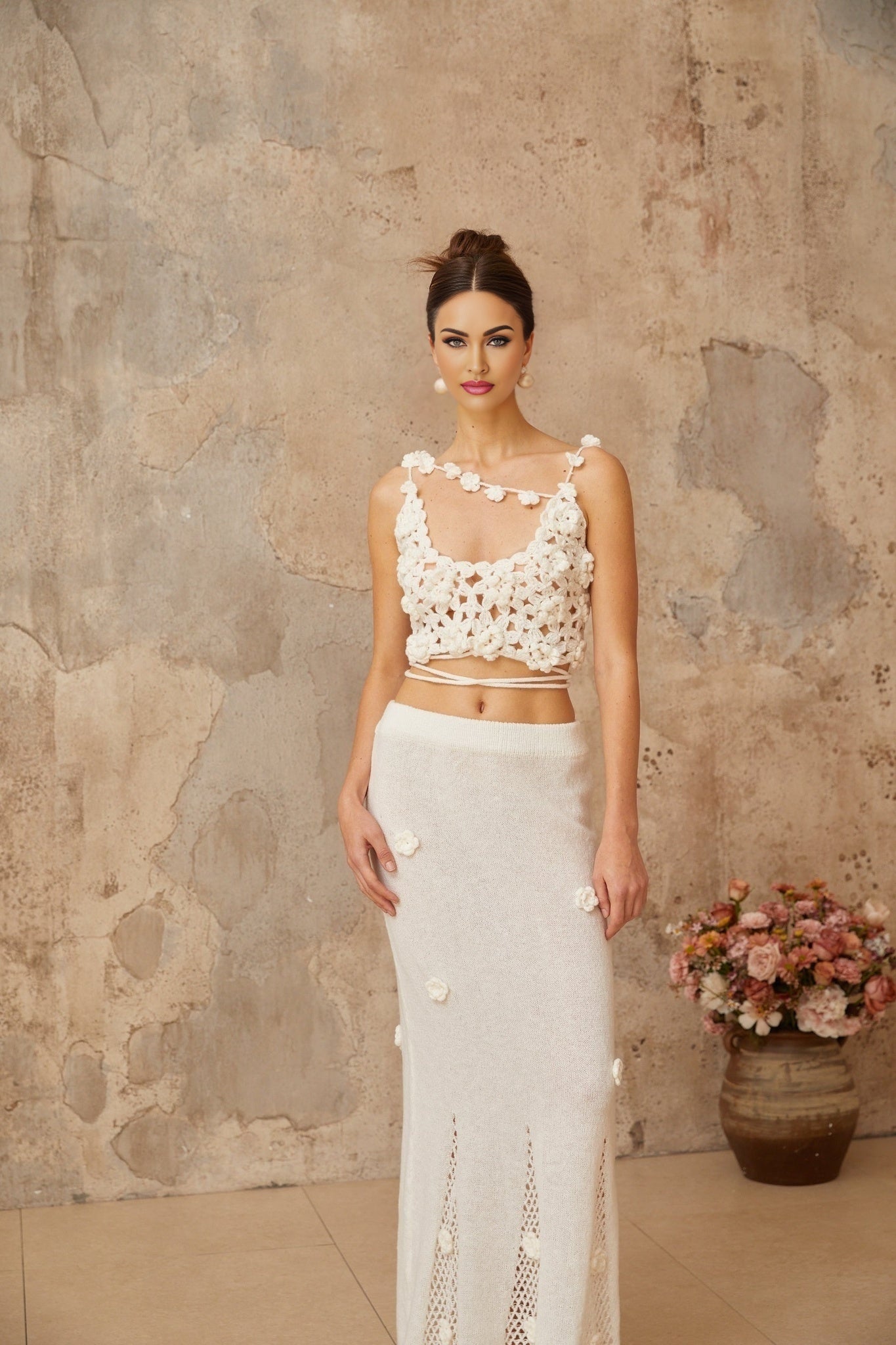 Woman wearing white two piece outfit with floral applique details on top and skirt