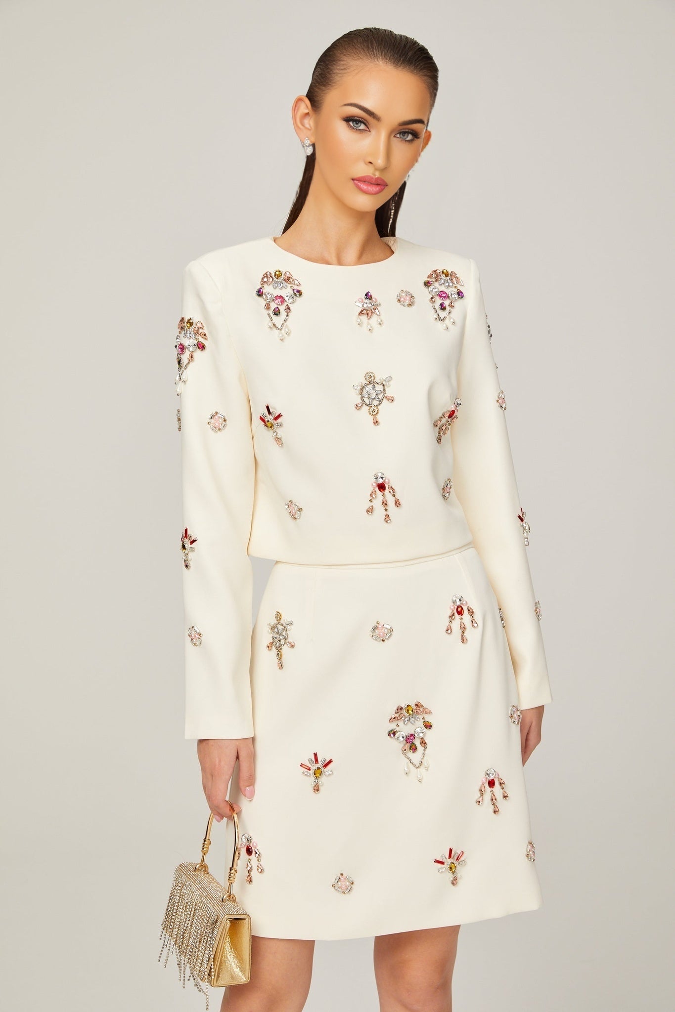 Woman wearing white twopiece outfit consisting of a crystalembellished top and matching skirt