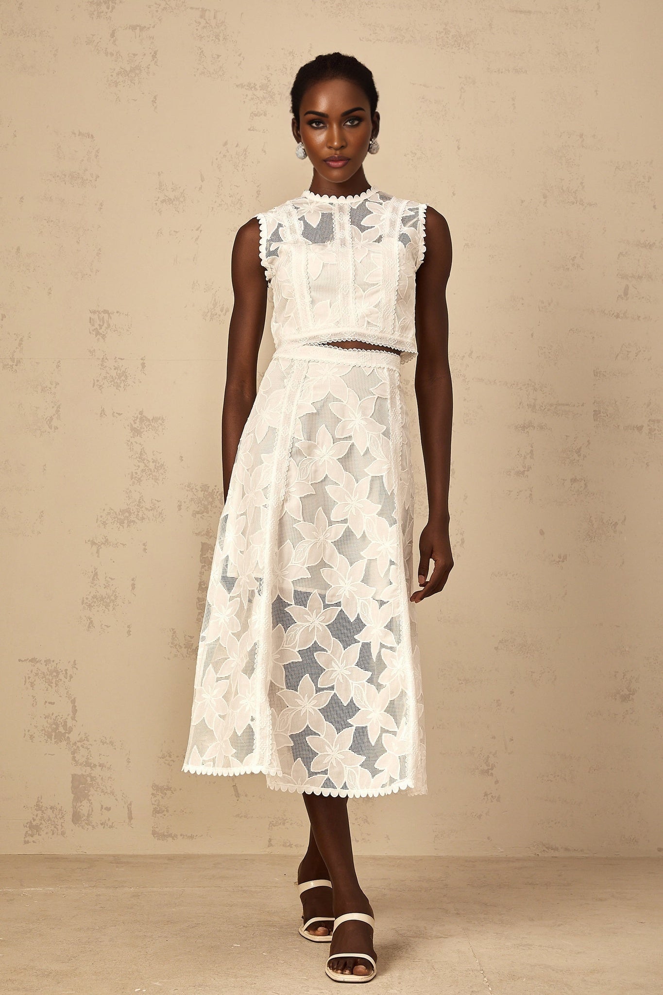 Woman wearing white twopiece set with floral embroidery featuring sleeveless top and matching skirt