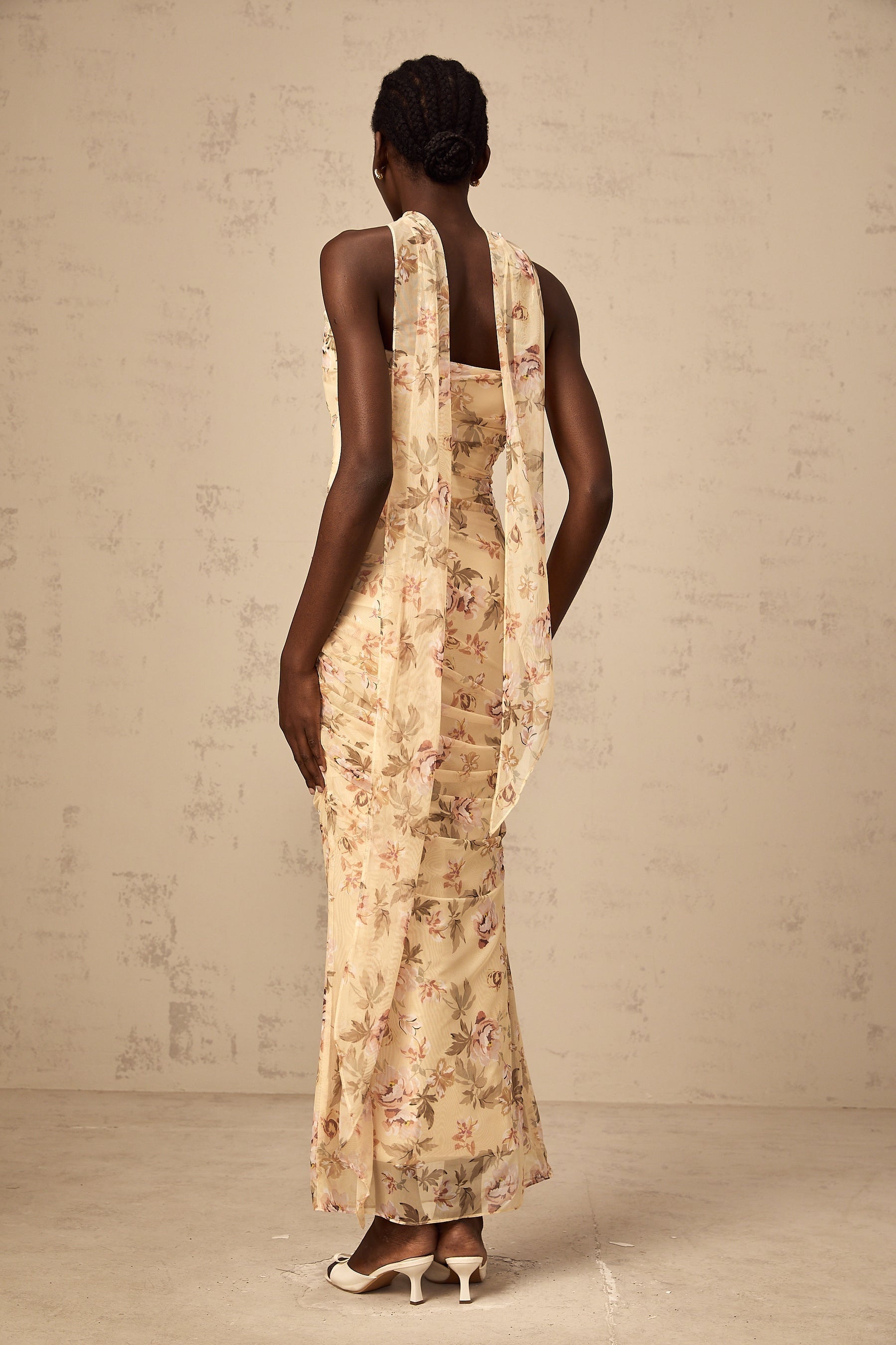 Woman wearing yellow floral print matching set with fitted top and skirt standing against white background