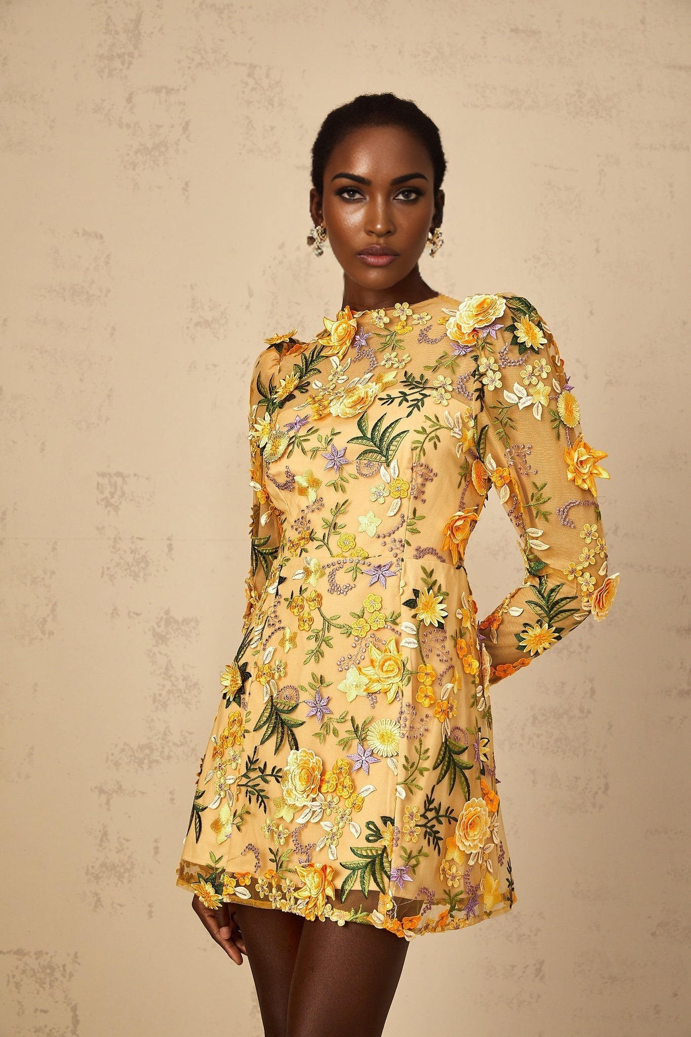 Woman wearing yellow mini dress with 3D floral applique details standing in neutral background