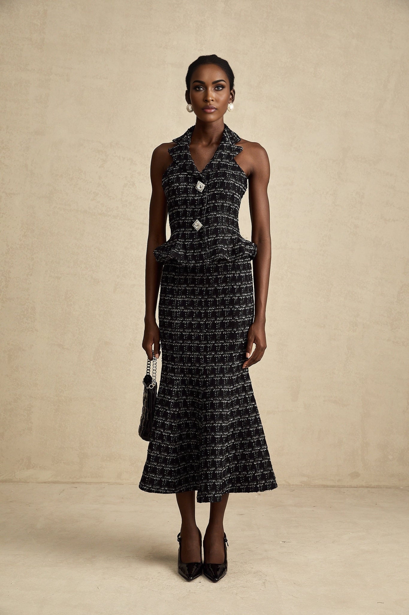 Young woman wearing a black and white checked tweed vest top and matching skirt set standing against a plain background
