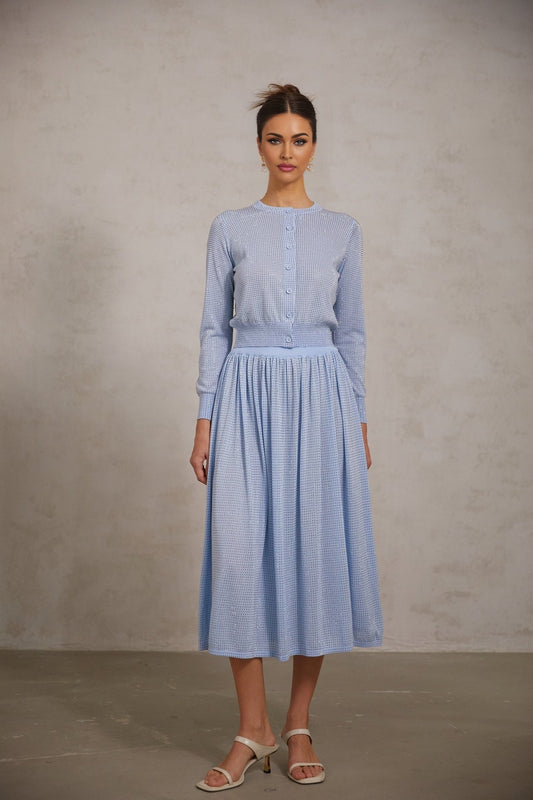 Young woman wearing a blue knitted top and skirt set decorated with rhinestones The top is sleeveless and the skirt is knee length Both pieces feature a ribbed texture and sparkle with embedded rhinestones