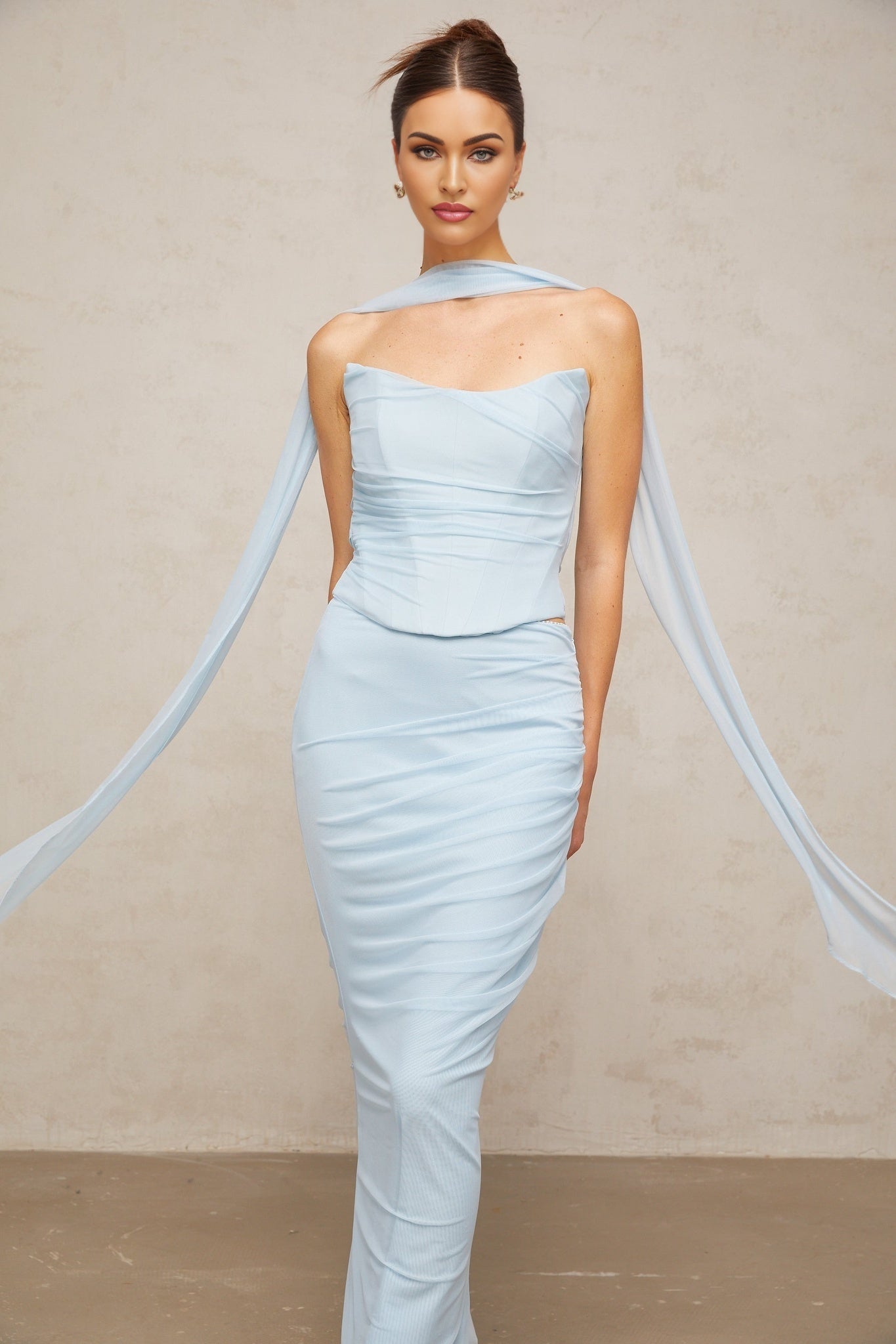 Young woman wearing a blue matching set consisting of a ruched tulle top and skirt The top features short sleeves and a fitted silhouette while the skirt has a flowy tulle design Both pieces are made from sheer blue fabric with ruching details