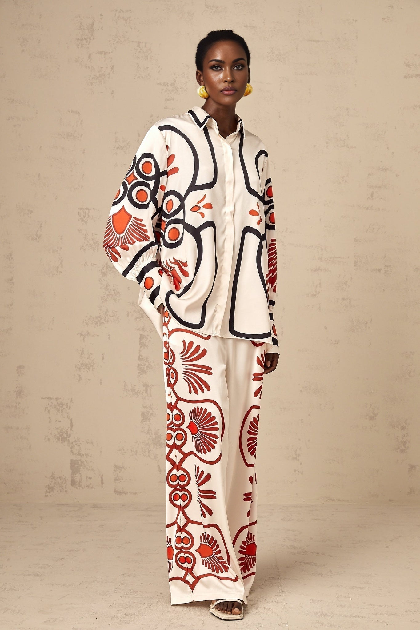 Young woman wearing a colorful floral print matching set consisting of a shirt and trousers standing in a relaxed pose against a plain background