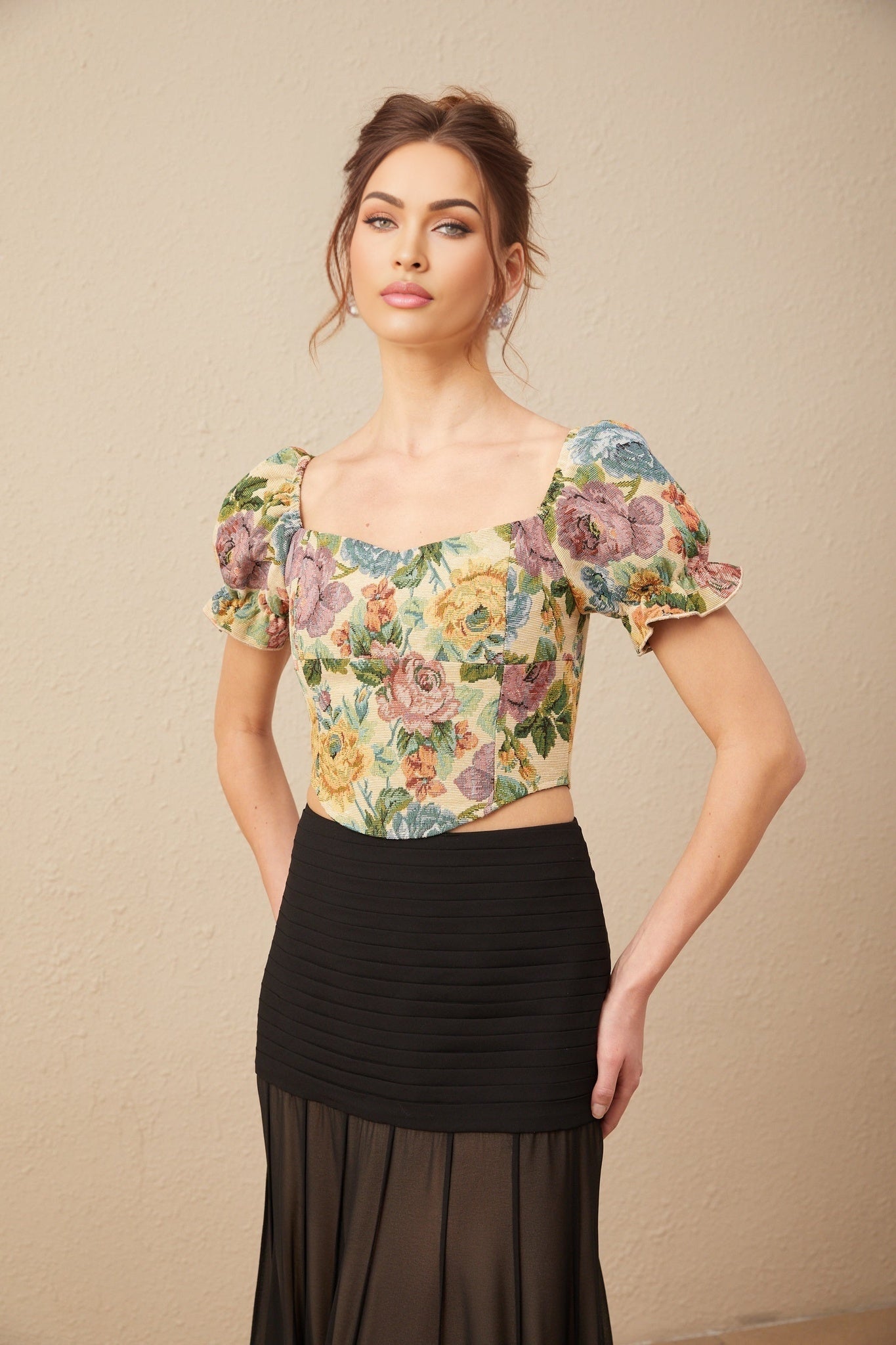 Young woman wearing a cropped floral print top with short puffed sleeves and a square neckline in vibrant colors against a plain background
