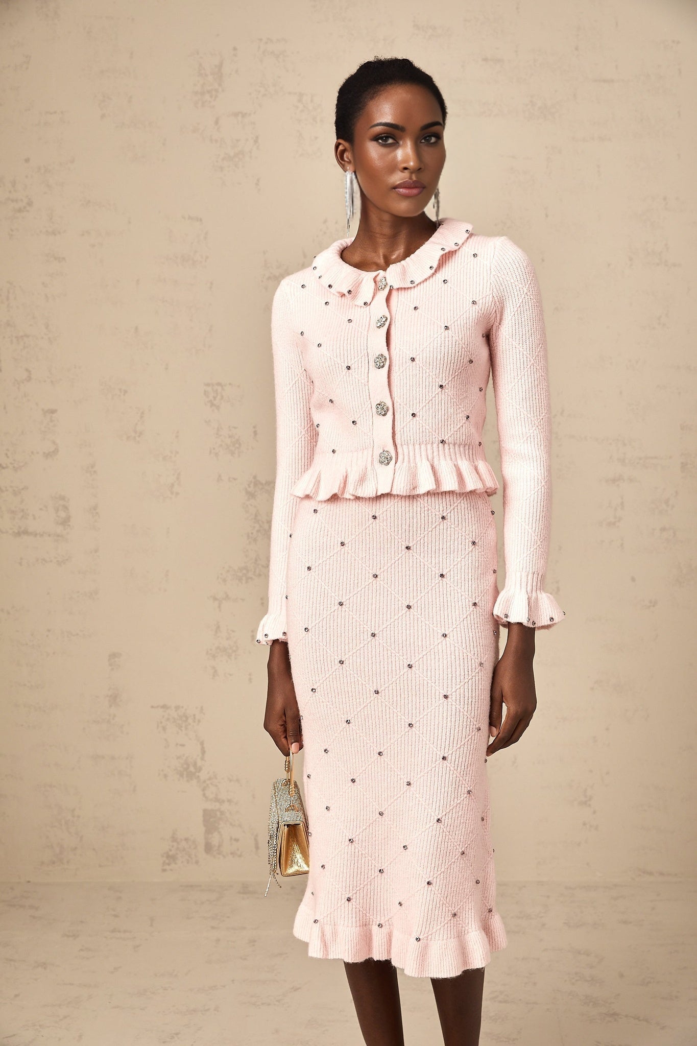 Young woman wearing a pink argyle patterned knit cardigan and matching skirt set against a plain background