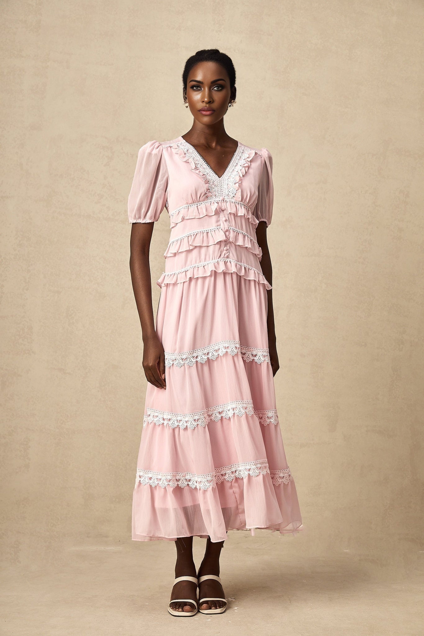 Young woman wearing a pink midi dress with ruffled tiers and a flowy silhouette standing against a plain background