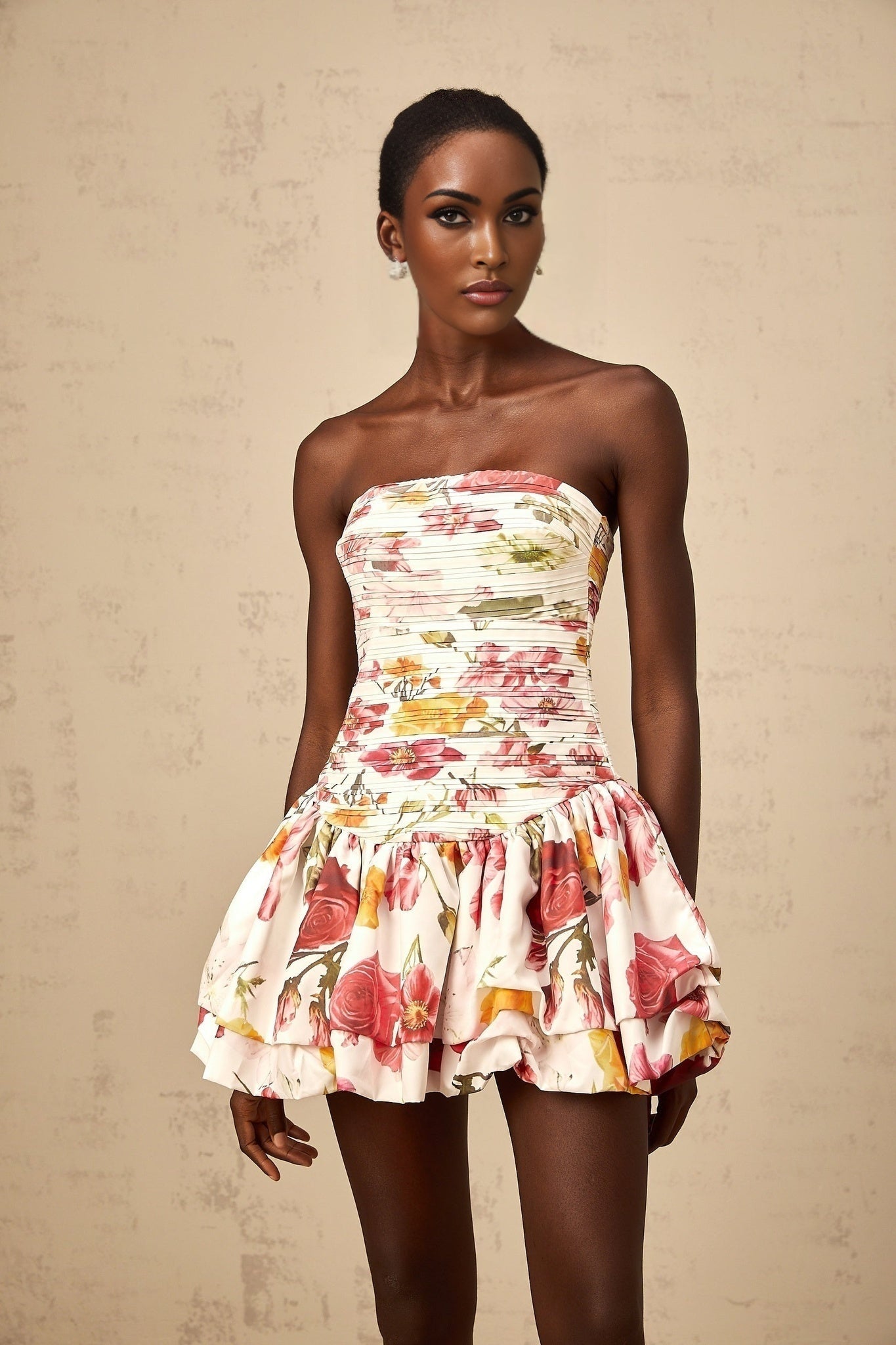 Young woman wearing a pink mini dress with floral print and smocked bodice standing in a sunlit garden