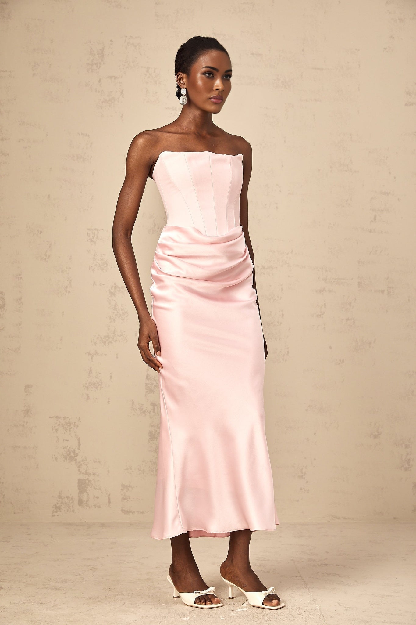 Young woman wearing a pink offshoulder maxi dress with flowing fabric standing in a garden setting