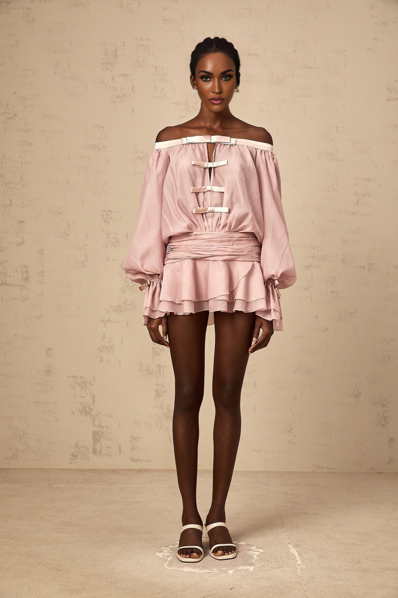 Young woman wearing a pink offshoulder mini dress with bow detail and ruffled hem