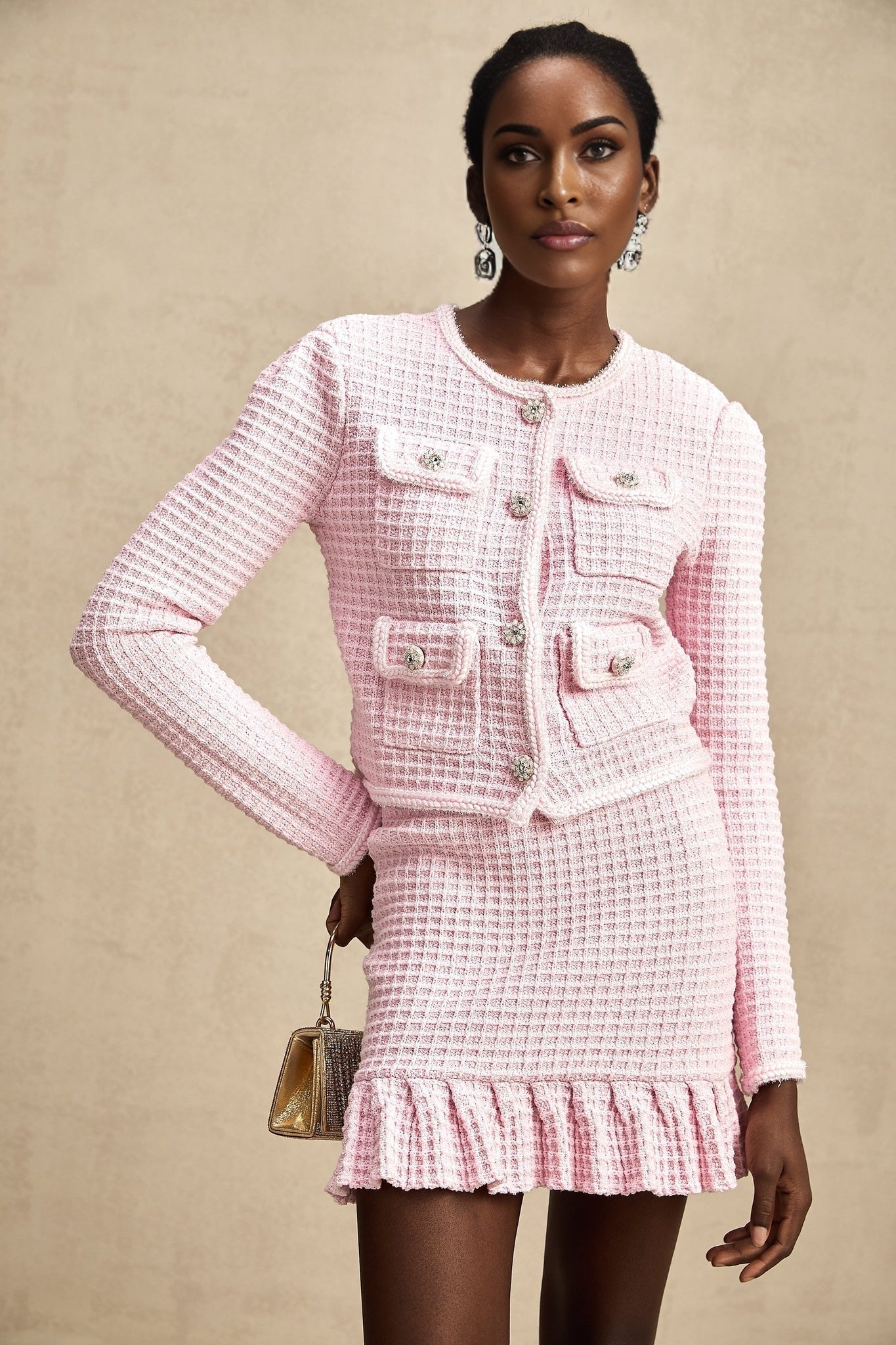 Young woman wearing a pink waffle knit jacket and matching skirt set standing against a plain background