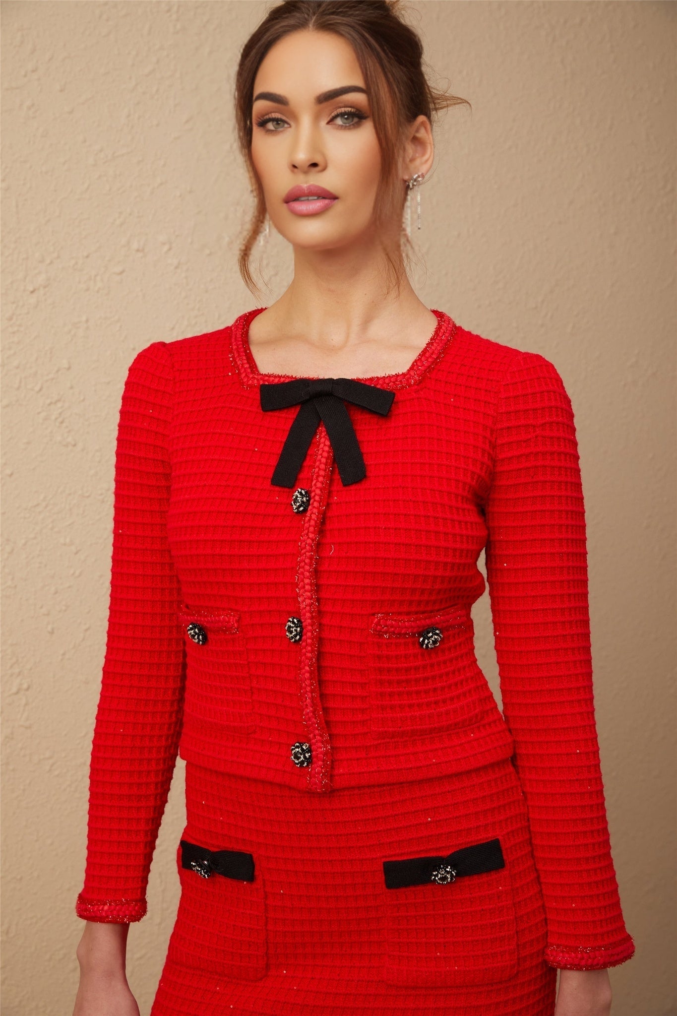 Young woman wearing a red braided waffle knit jacket and matching skirt set named Cynthia standing against a plain background