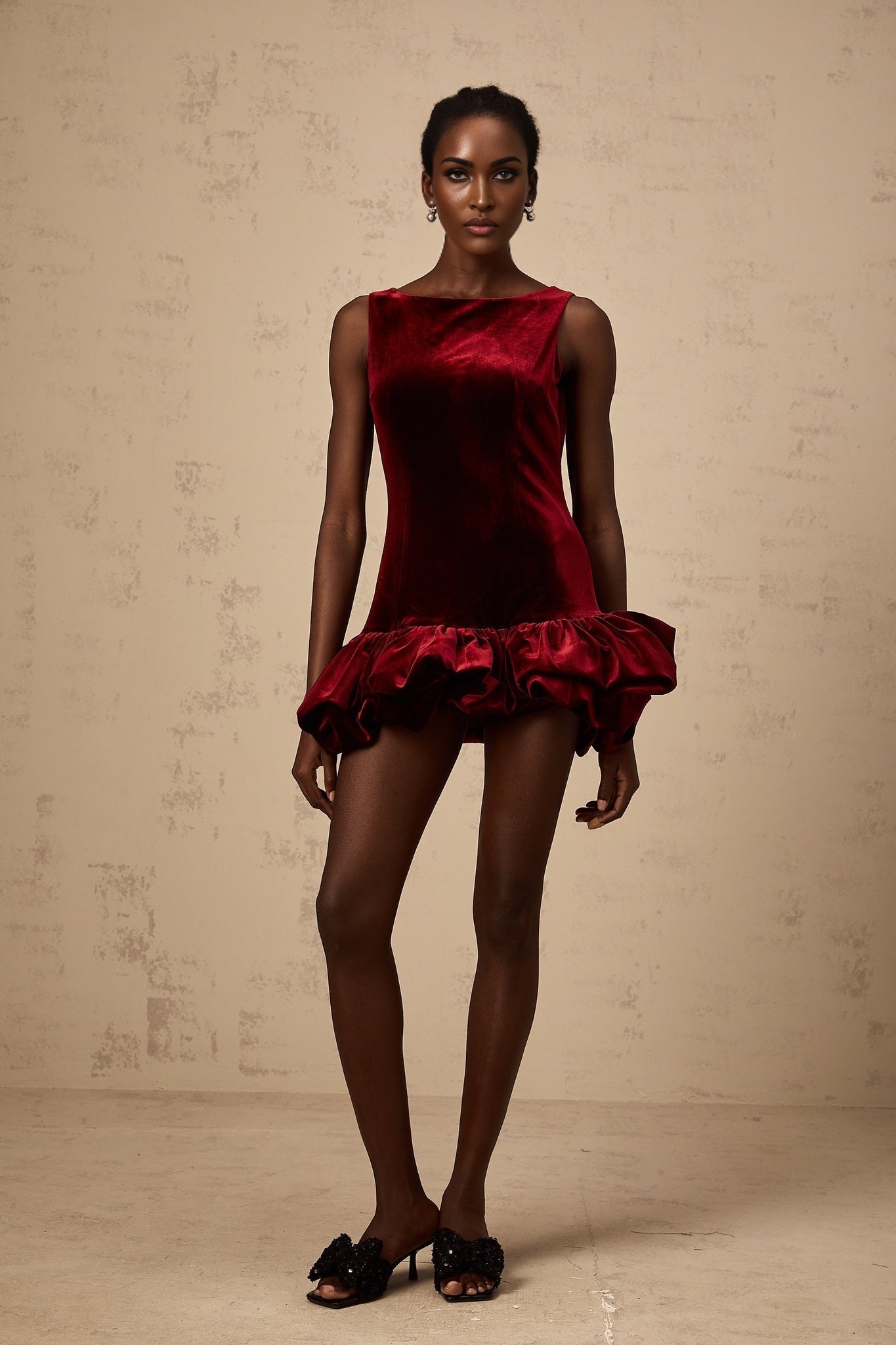Young woman wearing a red velvet mini dress with peplum hem detail standing against plain background