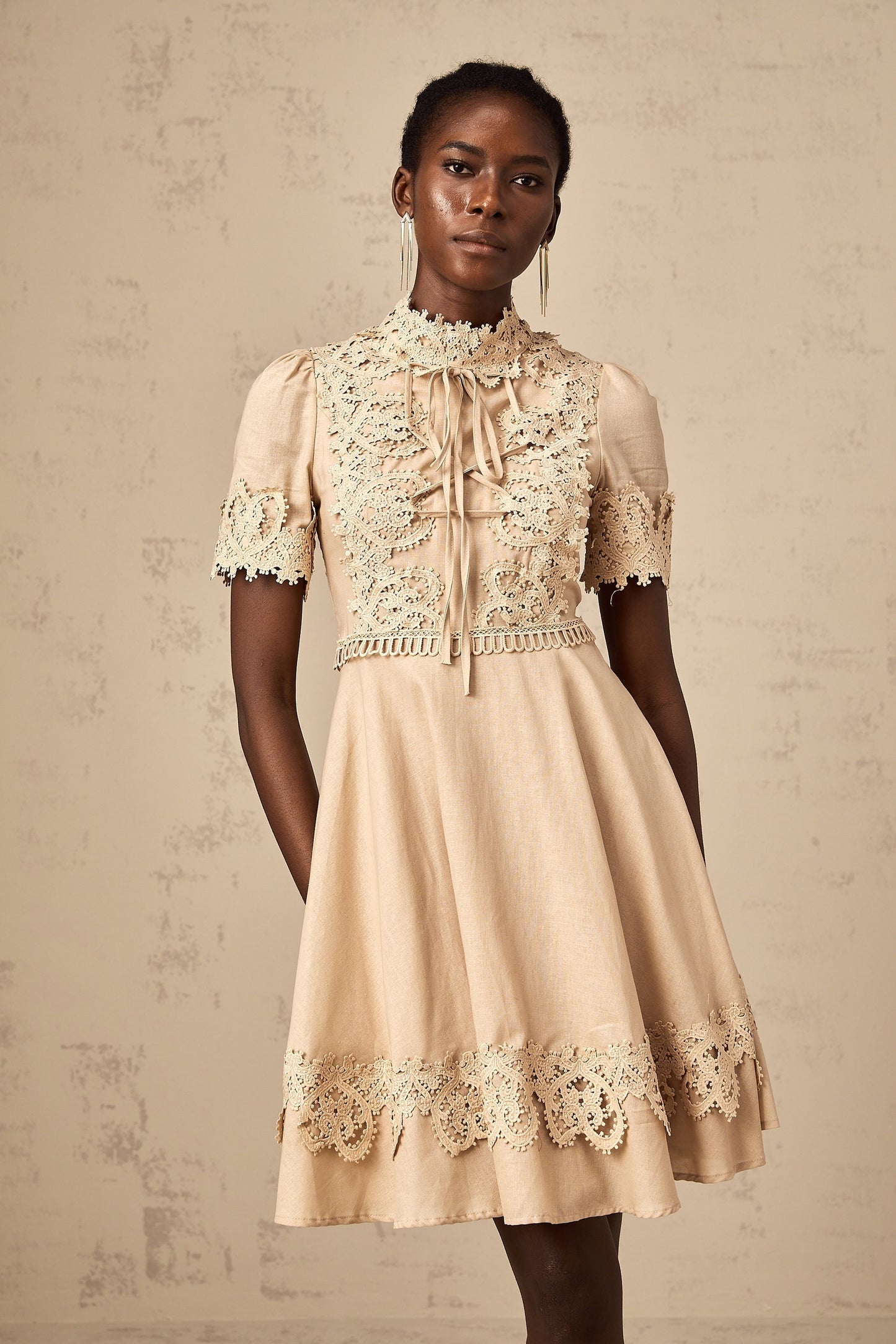 Young woman wearing a short flared dress with corded lace pattern and delicate straps standing against a plain background