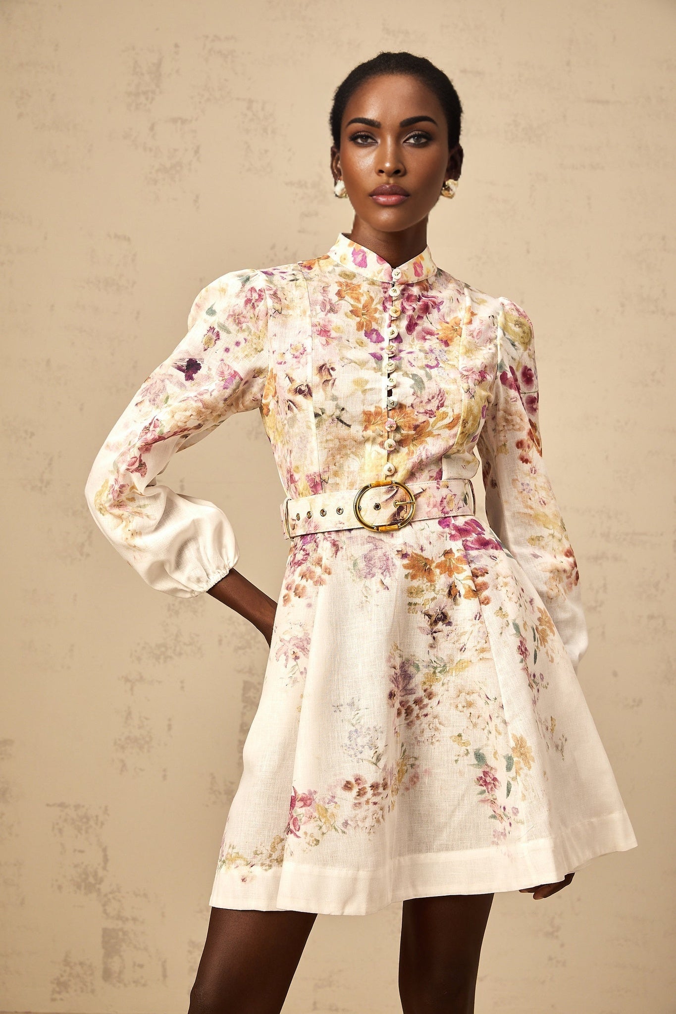 Young woman wearing a short floral print dress with vibrant colors and a flowy design standing against a plain background