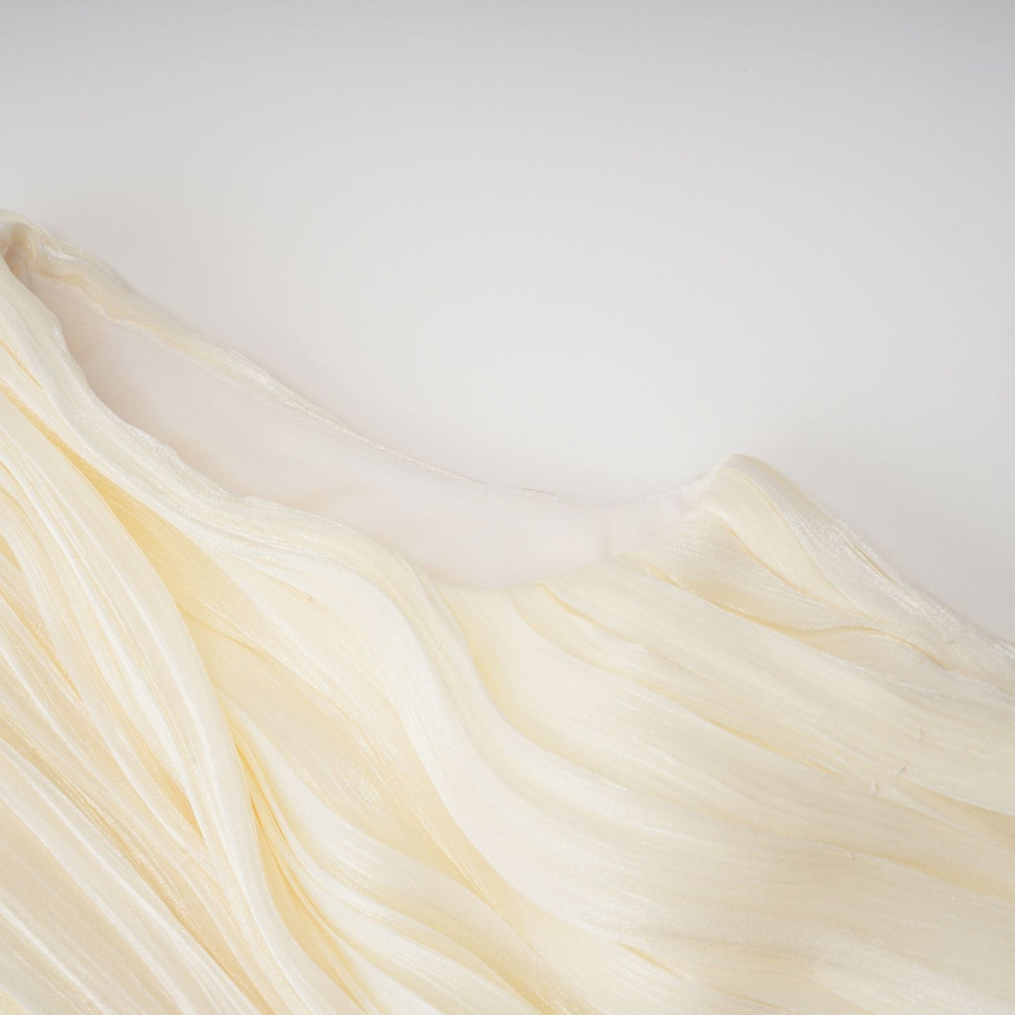 Young woman wearing a short pleated dress with ribbon accent standing in front of a plain background