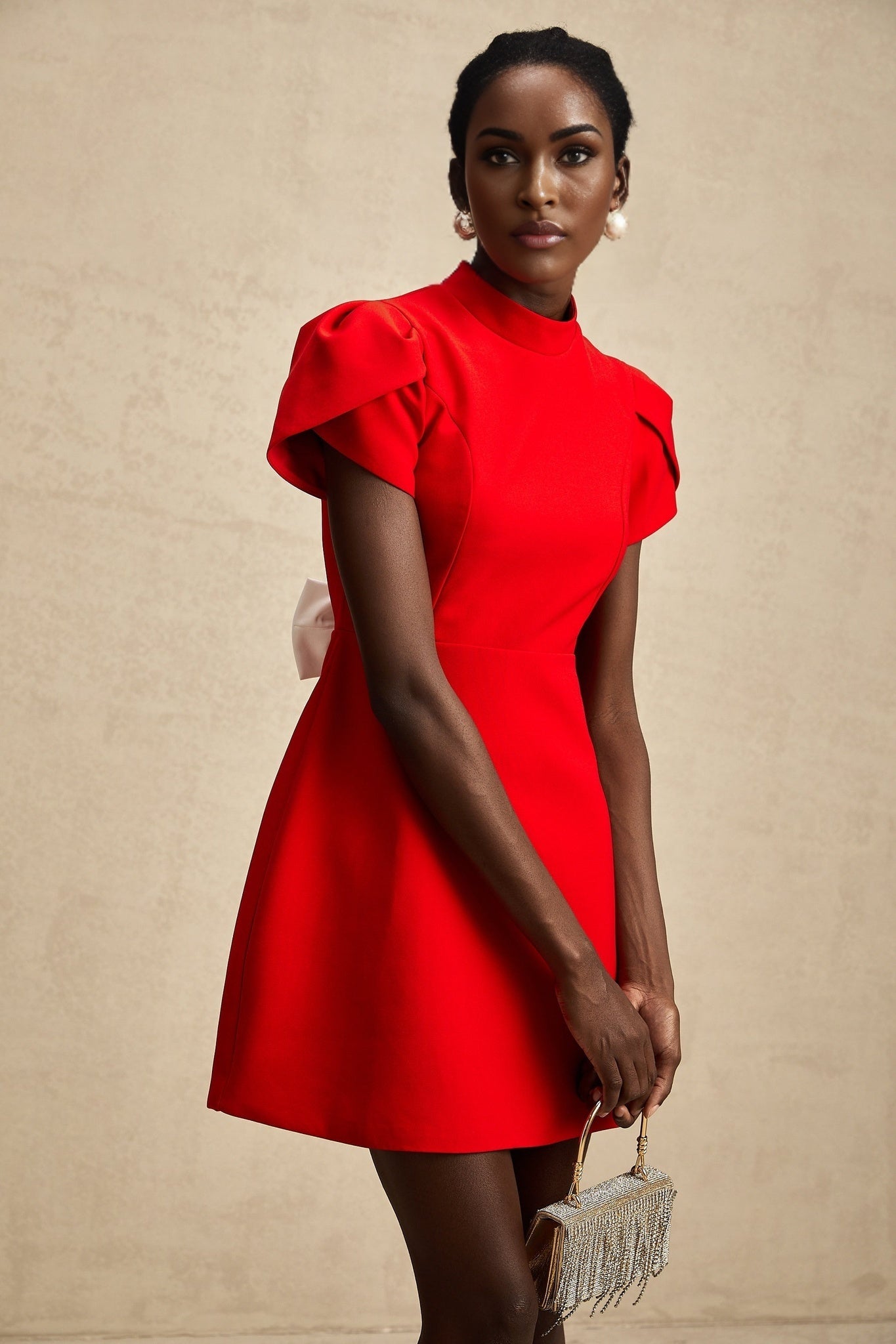 Young woman wearing a short red dress with petal sleeves and a cutout detail with a bow accent