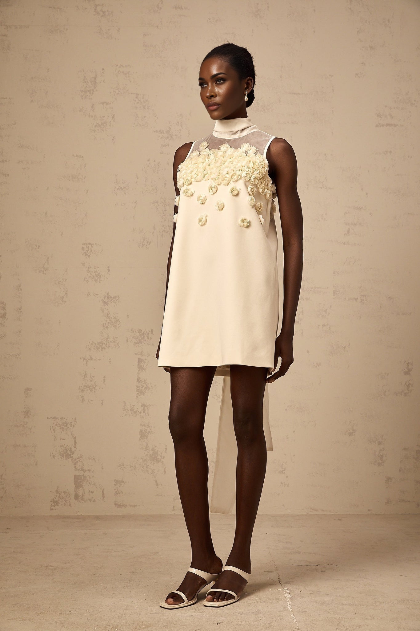 Young woman wearing a sleeveless mini dress with a floral pattern standing in a casual pose against a plain background