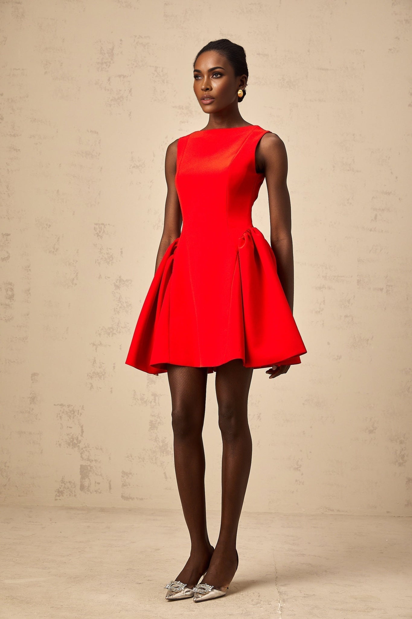 Young woman wearing a vibrant red sleeveless mini dress with a flared skirt standing against a plain background
