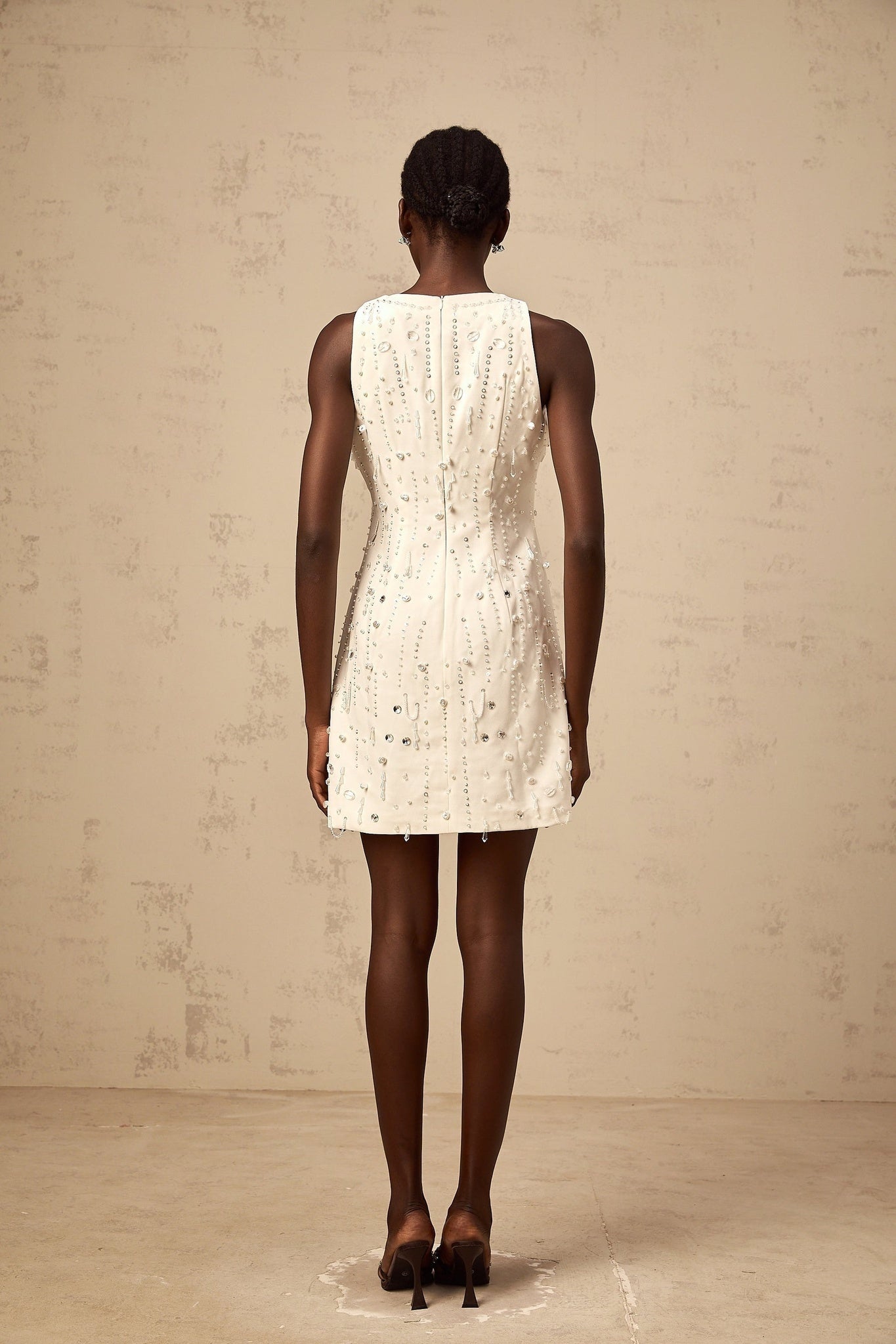 Young woman wearing a white Aline mini dress with embellishments standing in a neutral background