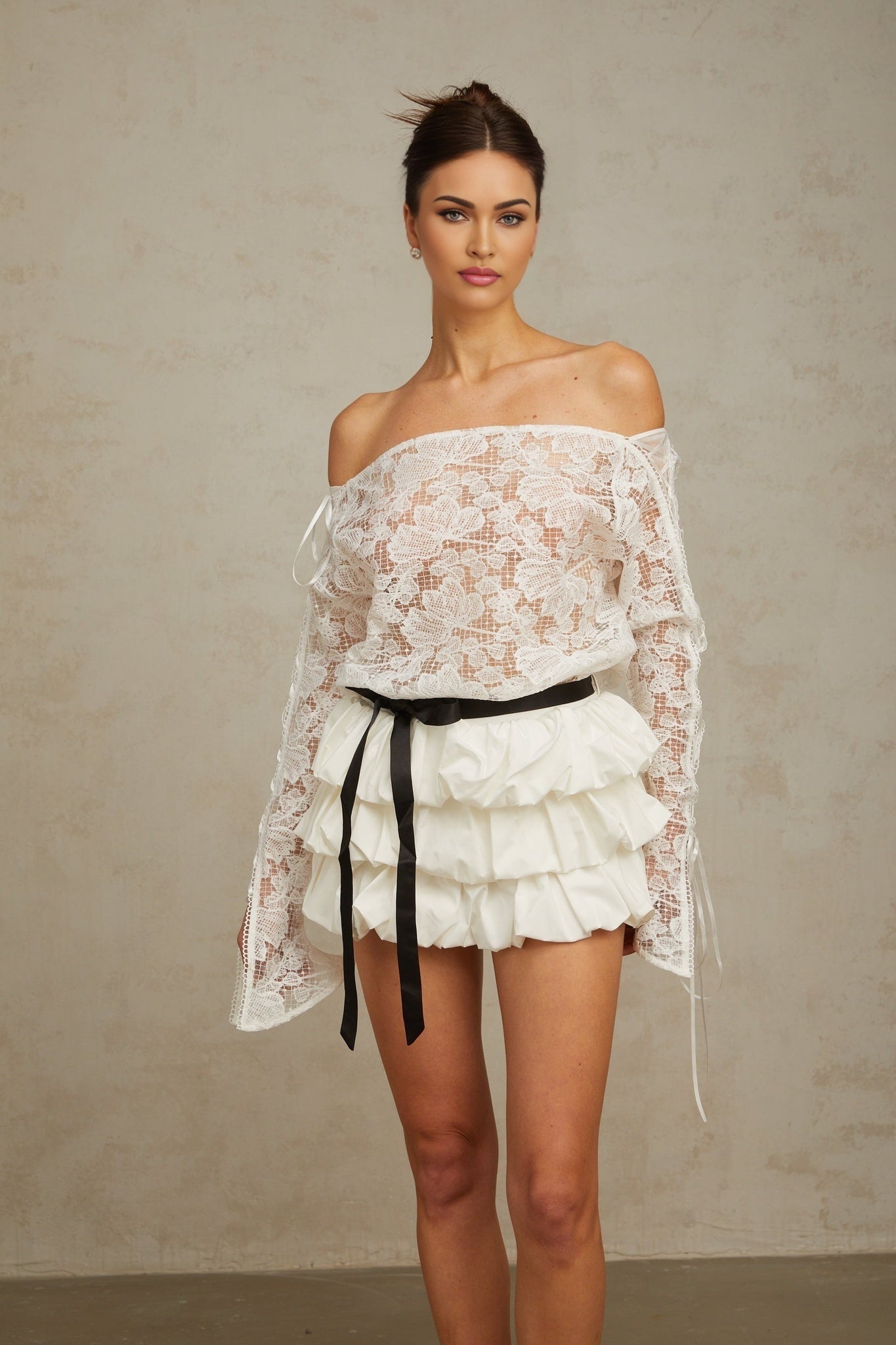 Young woman wearing a white floral lace matching set consisting of a sleeveless top and short skirt standing against a plain background