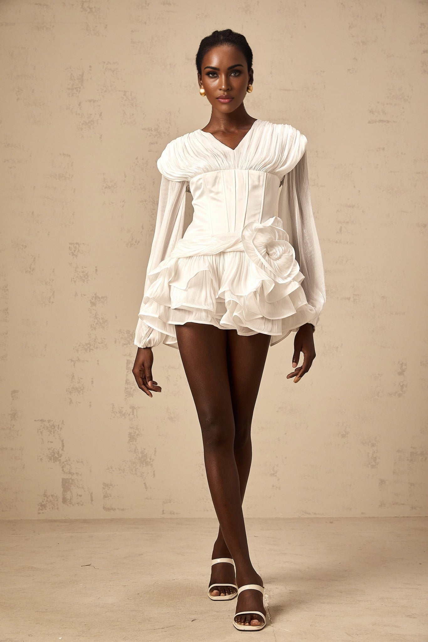 Young woman wearing a white fully pleated mini dress with cinched waist detail standing against a plain background