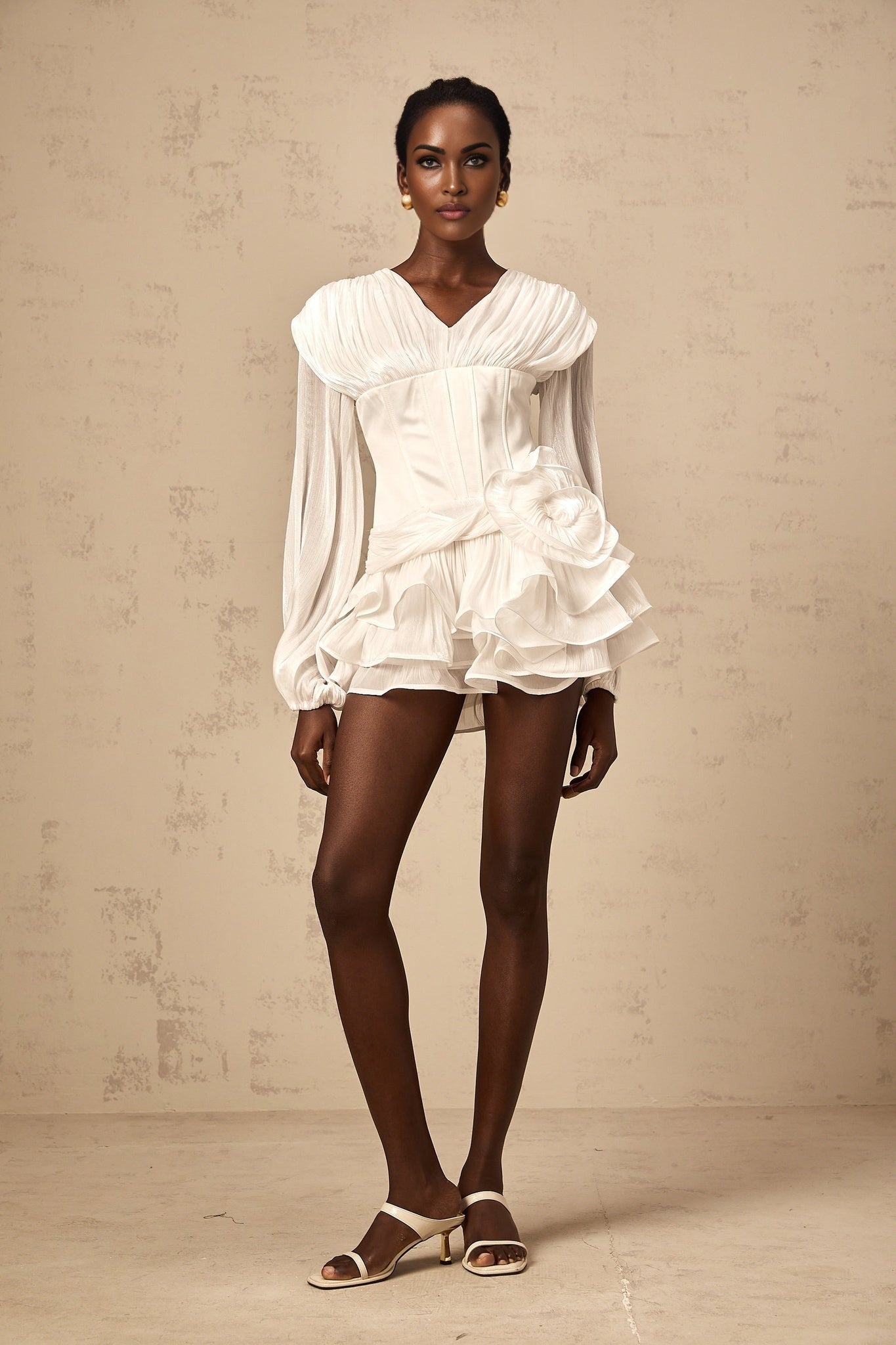 Young woman wearing a white fully pleated mini dress with cinched waist standing in front of neutral background