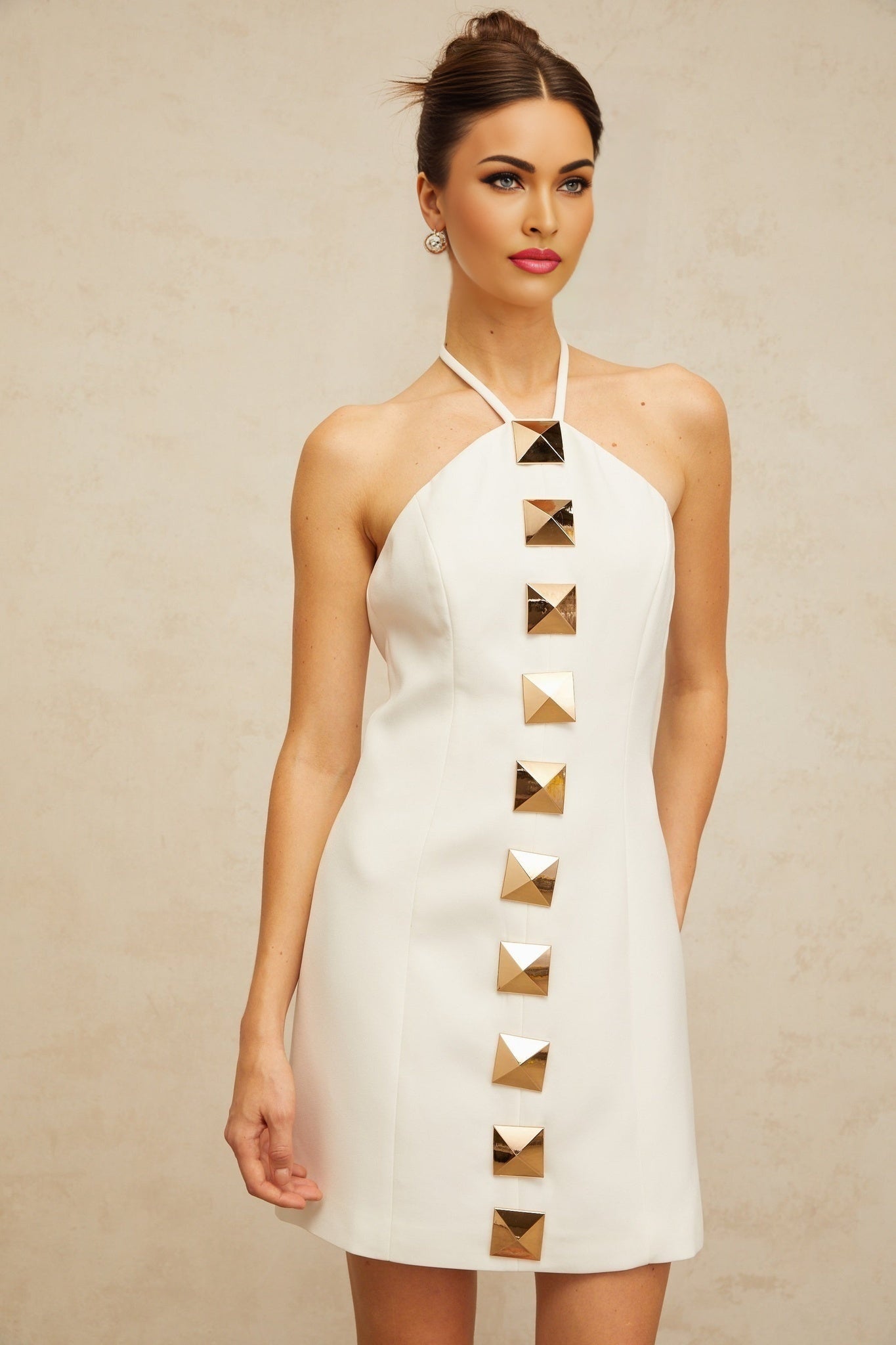 Young woman wearing a white halterneck mini dress with an Aline silhouette standing against a plain background