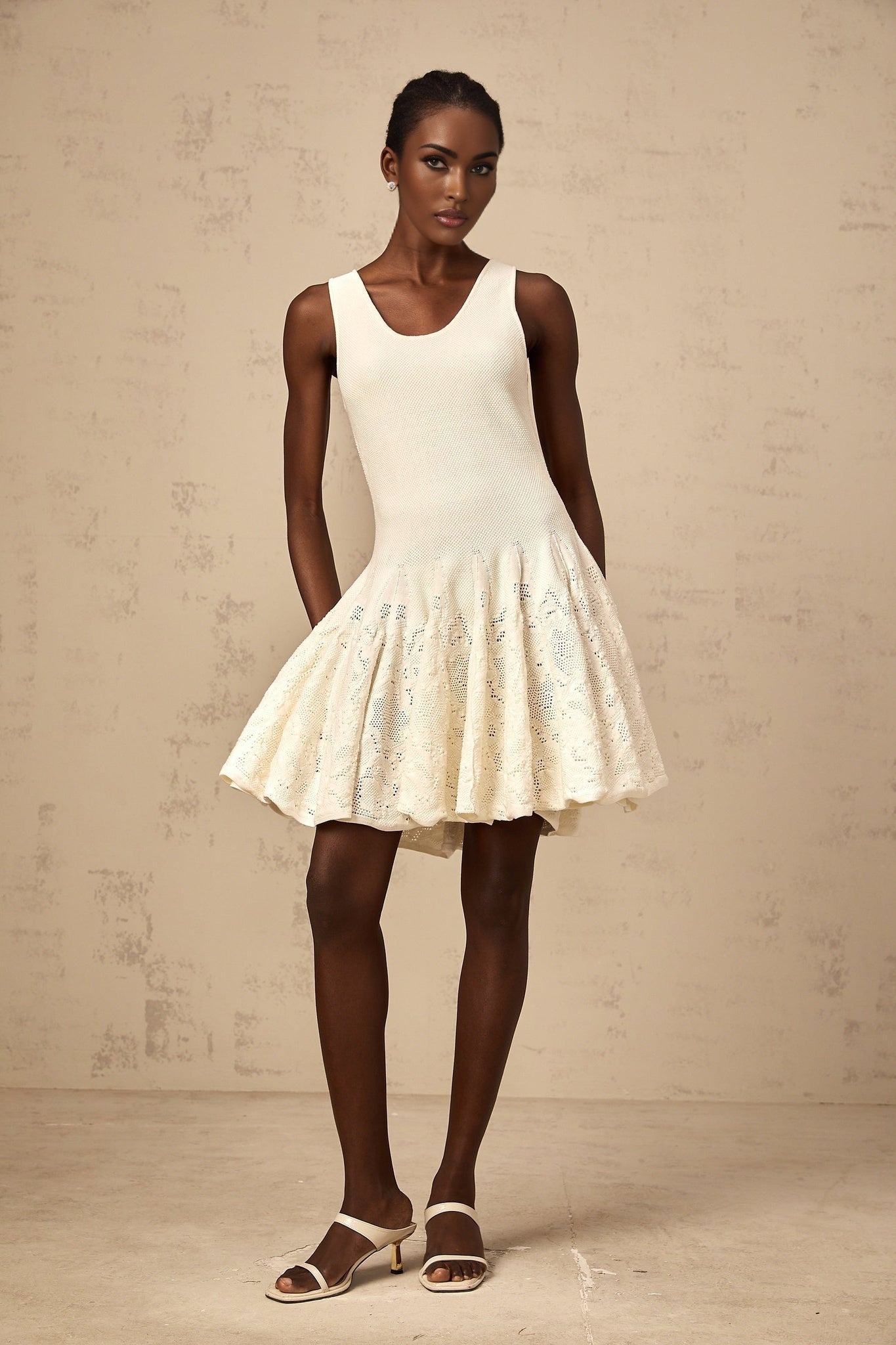 Young woman wearing a white jacquard knit mini dress with textured pattern standing against neutral background