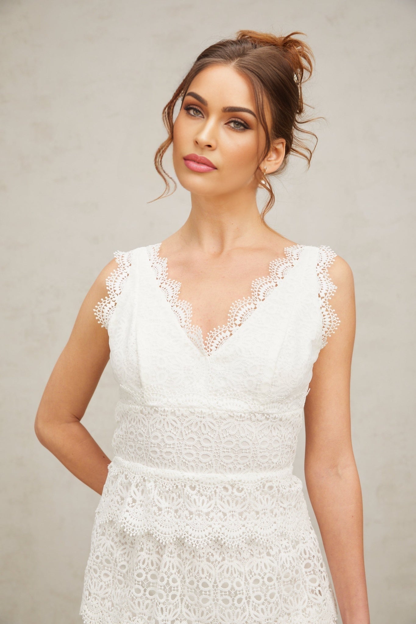Young woman wearing a white lace tiered mini dress with short sleeves standing against a plain background