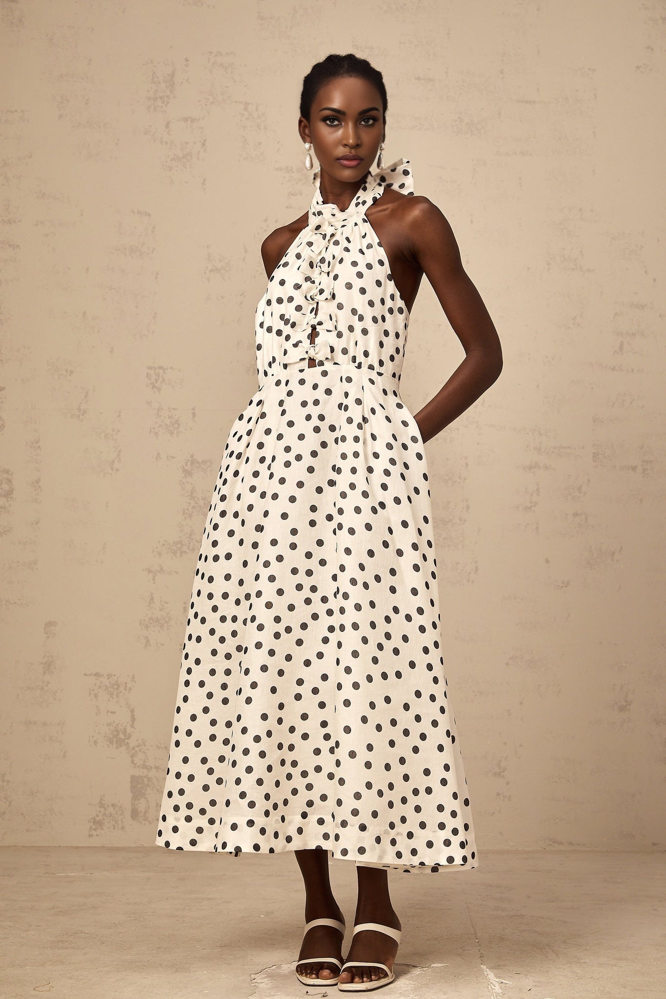 Young woman wearing a white midi dress with black polka dots and a large bow accent at the waist