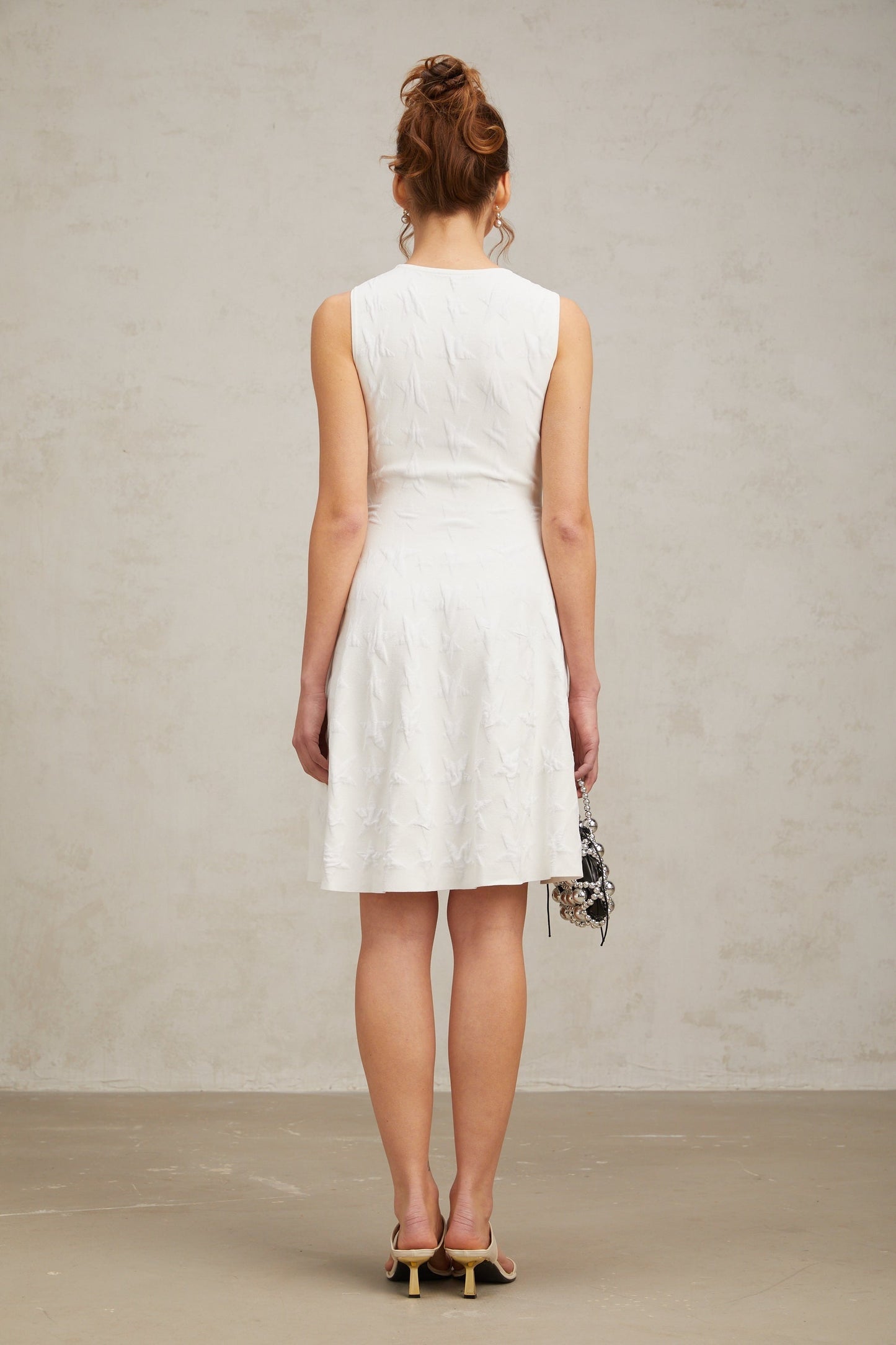 Young woman wearing a white mini dress with a star pattern knitted design and jasmineinspired details