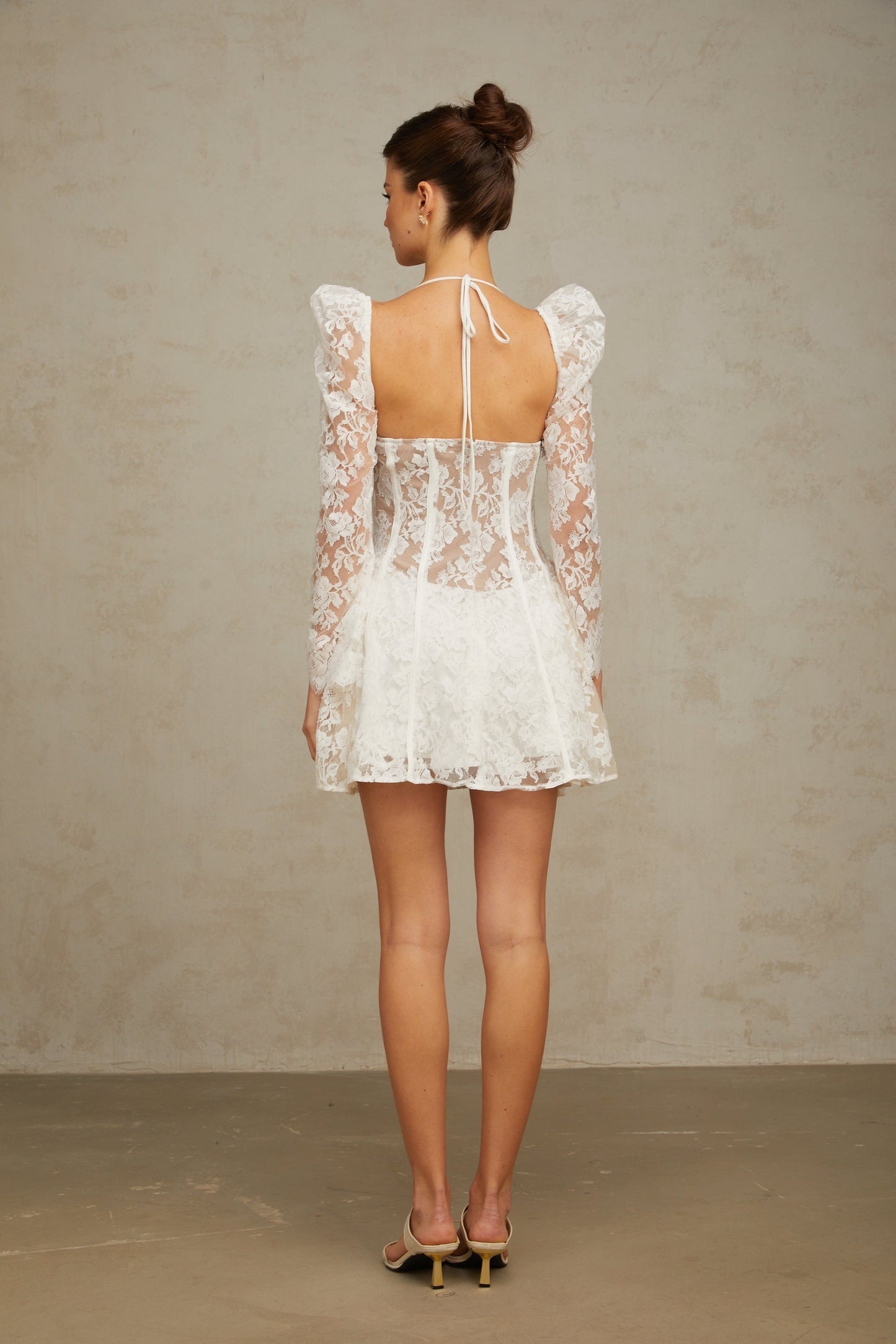 Young woman wearing a white mini dress with floral lace pattern and corset style bodice