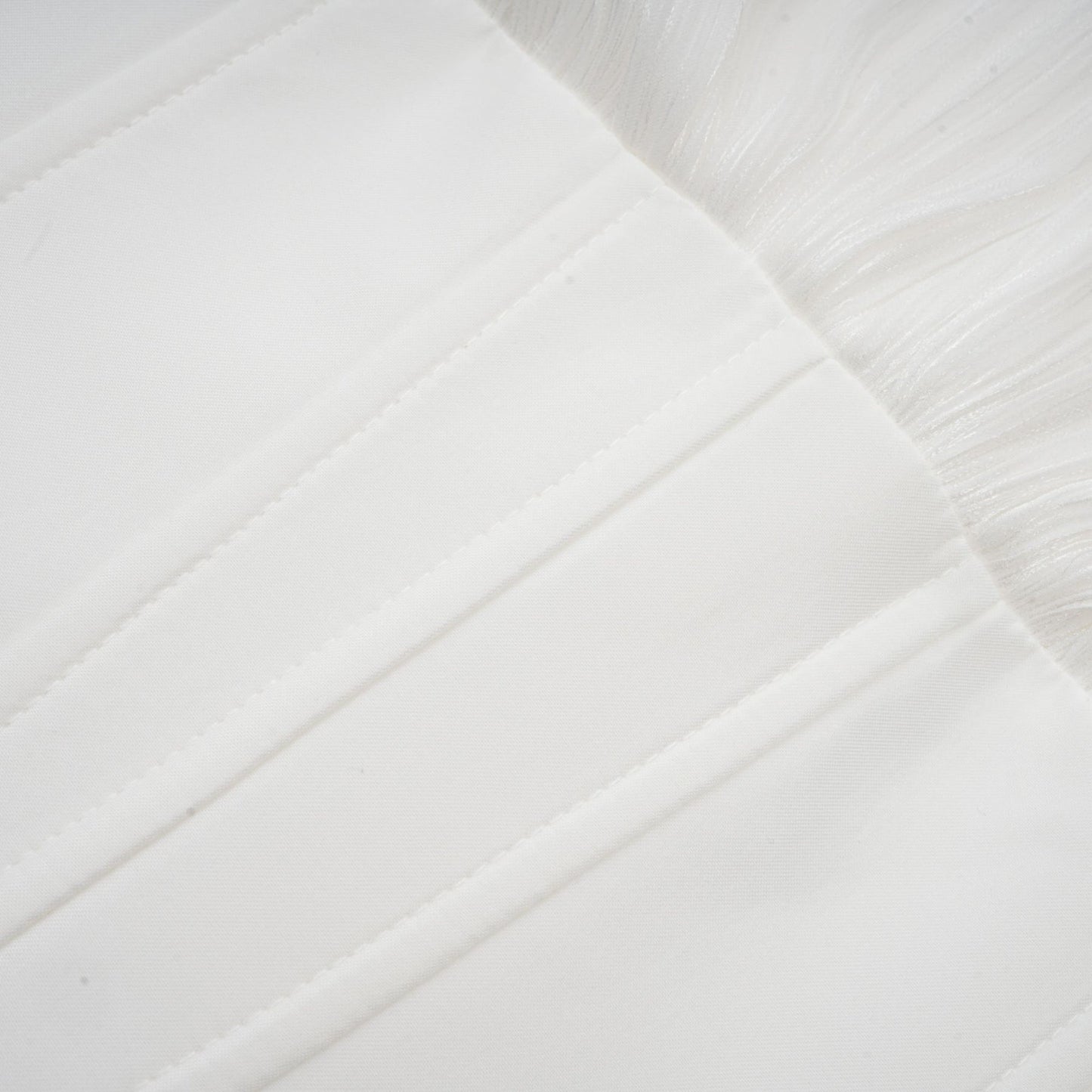 Young woman wearing a white pleated mini dress with cinched waist standing against a plain background