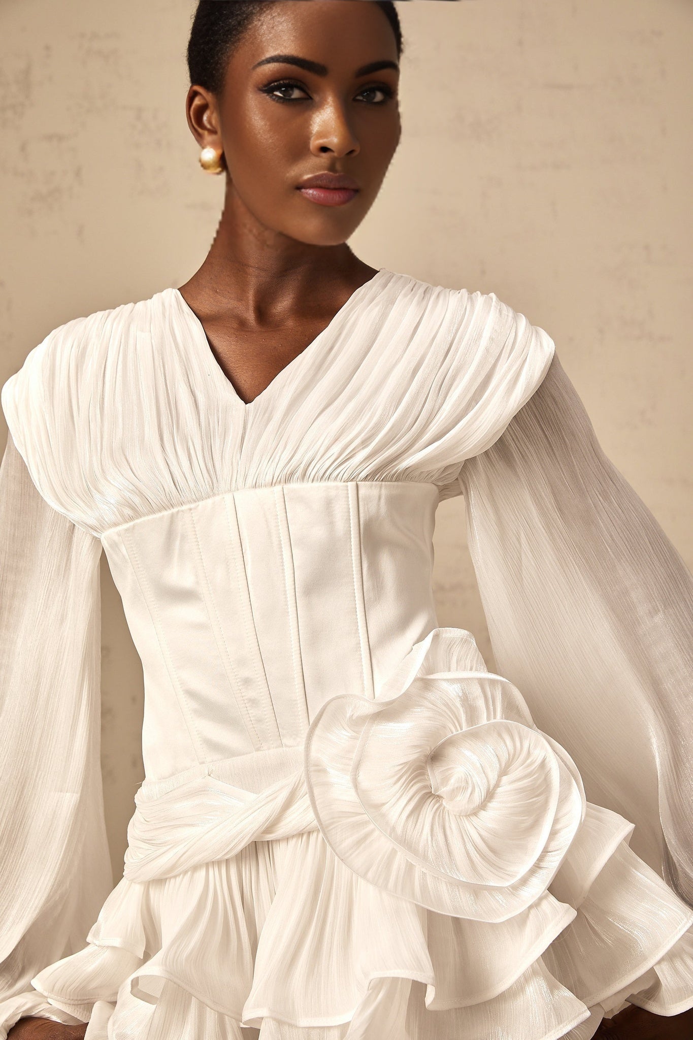 Young woman wearing a white pleated mini dress with cinched waist standing against neutral background