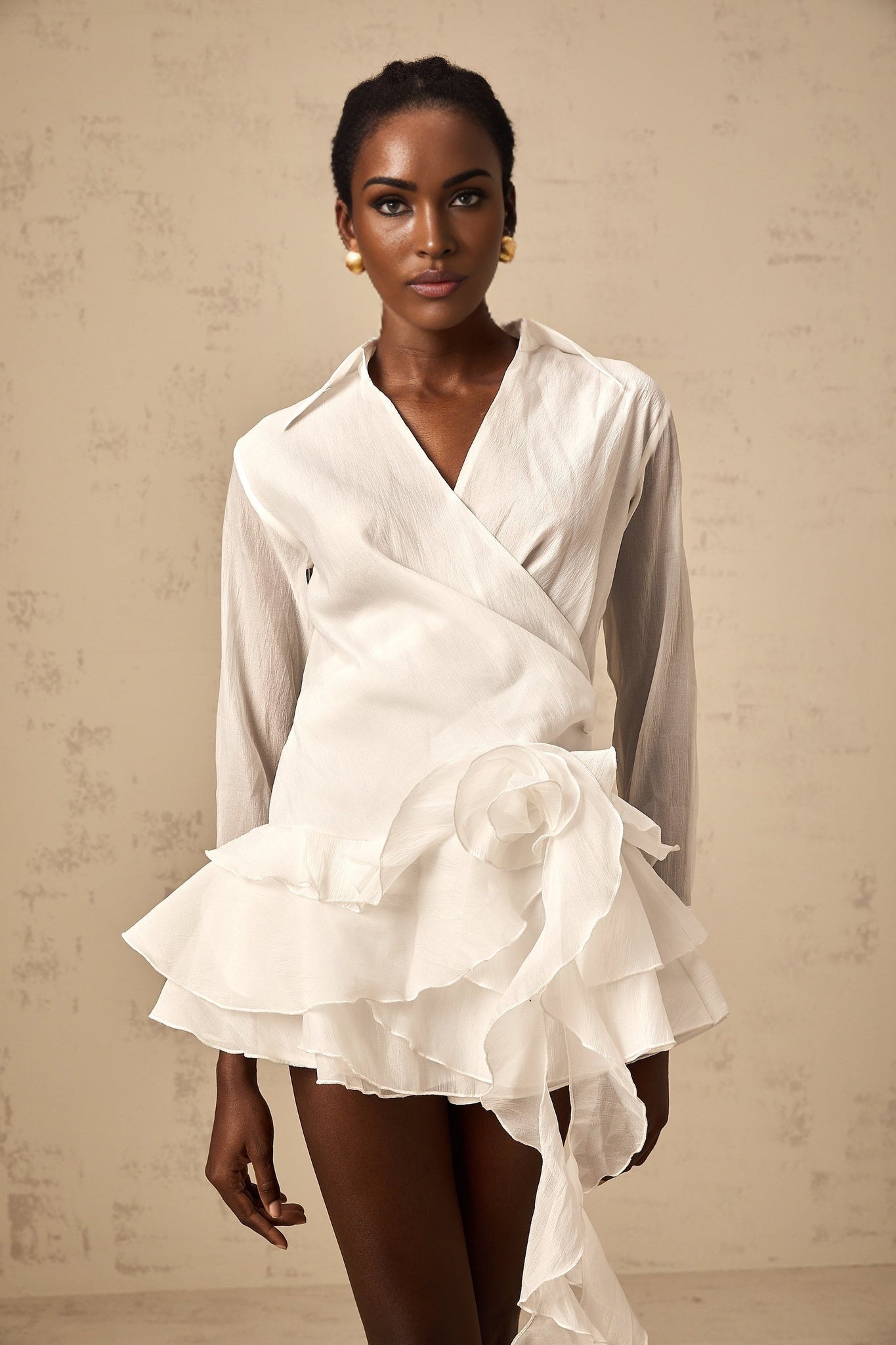 Young woman wearing a white semi sheer mini dress with floral pattern and ruffled details standing in a natural outdoor setting