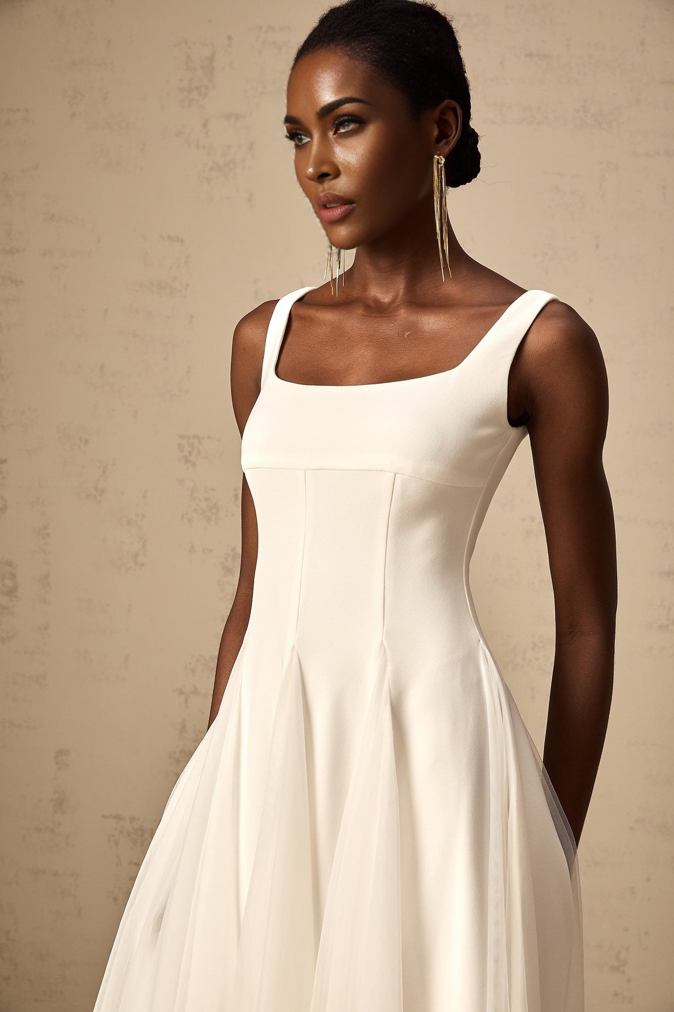 Young woman wearing a white tulle midi dress with godet inserts standing in a relaxed pose against a neutral background