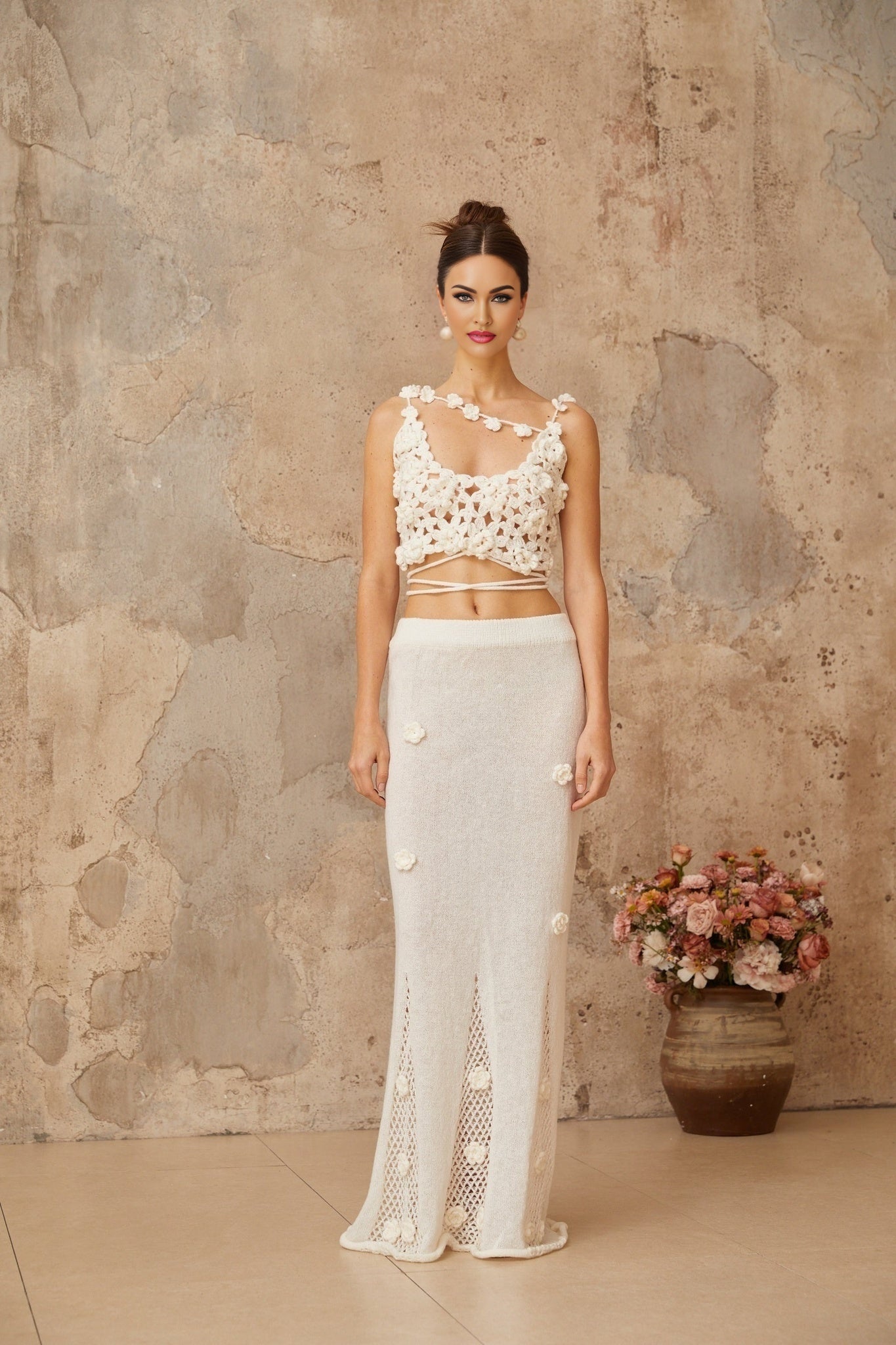 Young woman wearing a white twopiece outfit consisting of a sleeveless top and skirt with floral applique details