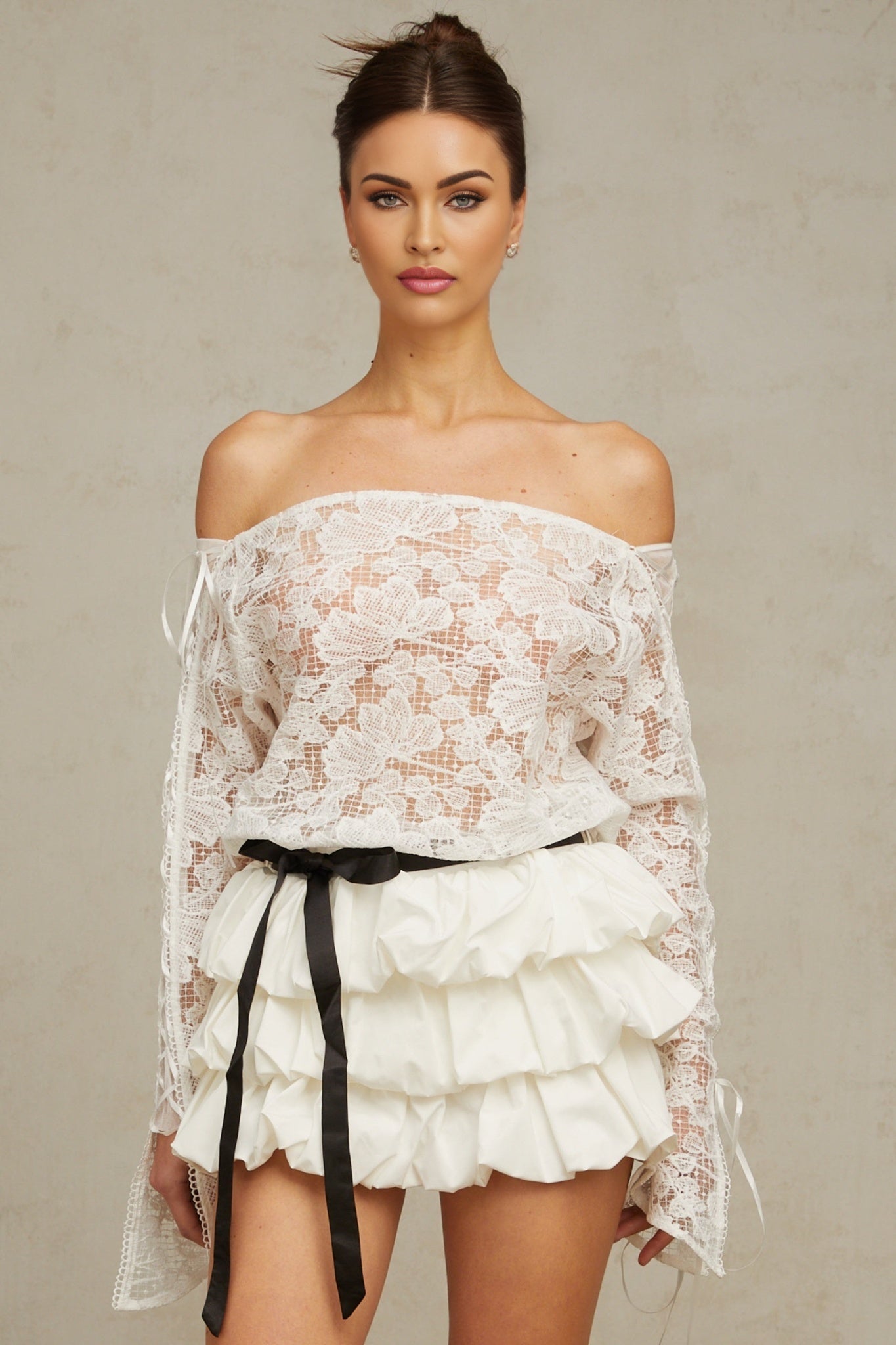 Young woman wearing white floral lace matching top and skirt set against plain background